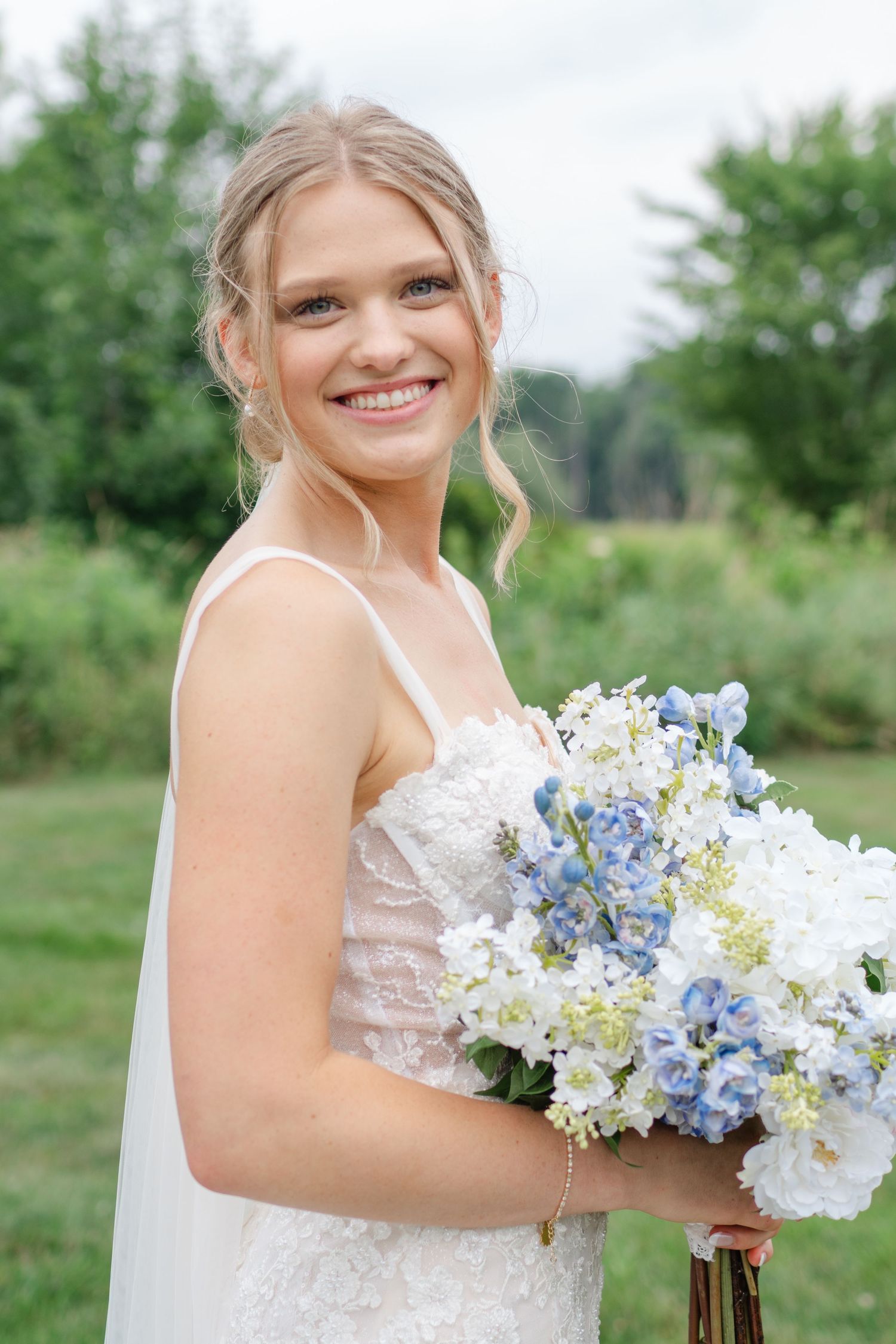 Joyful bride holds a stunning bouquet of blue and white hydrangeas in an outdoor setting.
