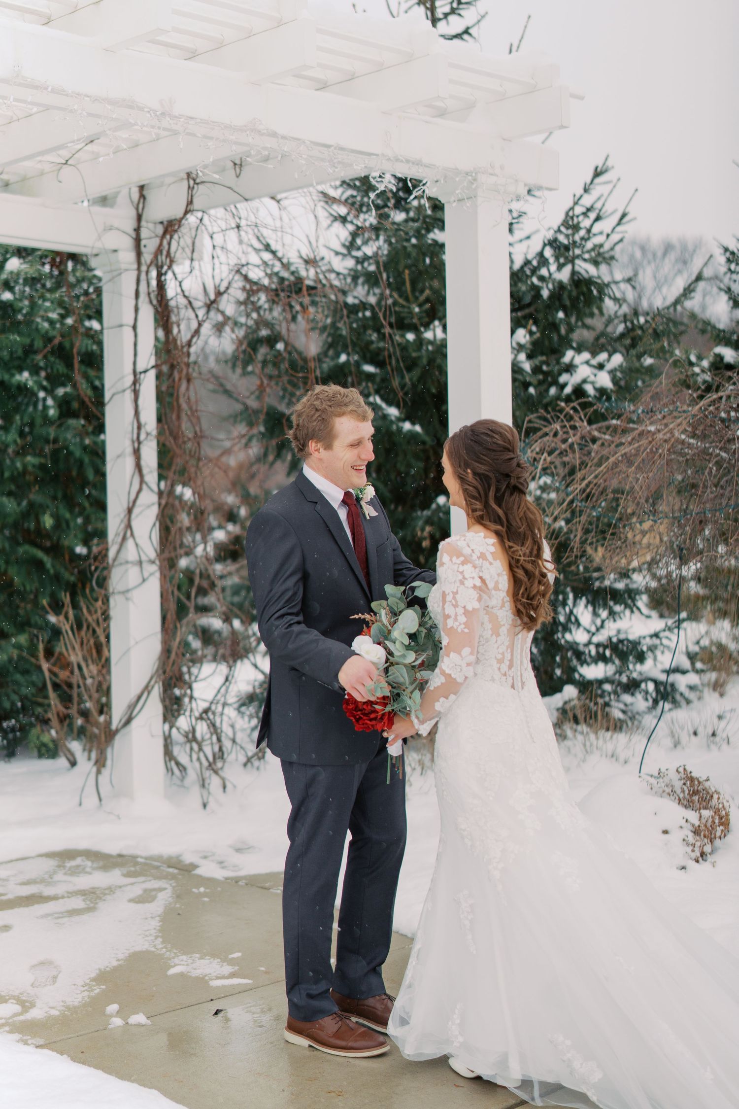 Bride and groom share intimate moment on snow-covered walkway surrounded by winter landscape.