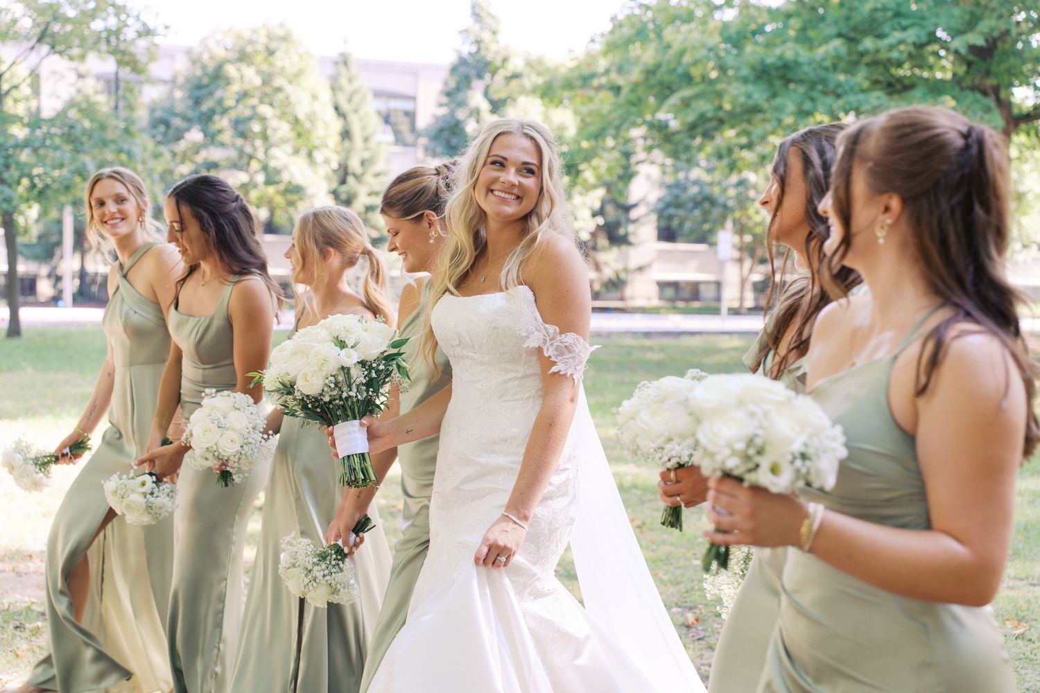 Wedding party in mint green dresses and white gowns celebrating outdoors.