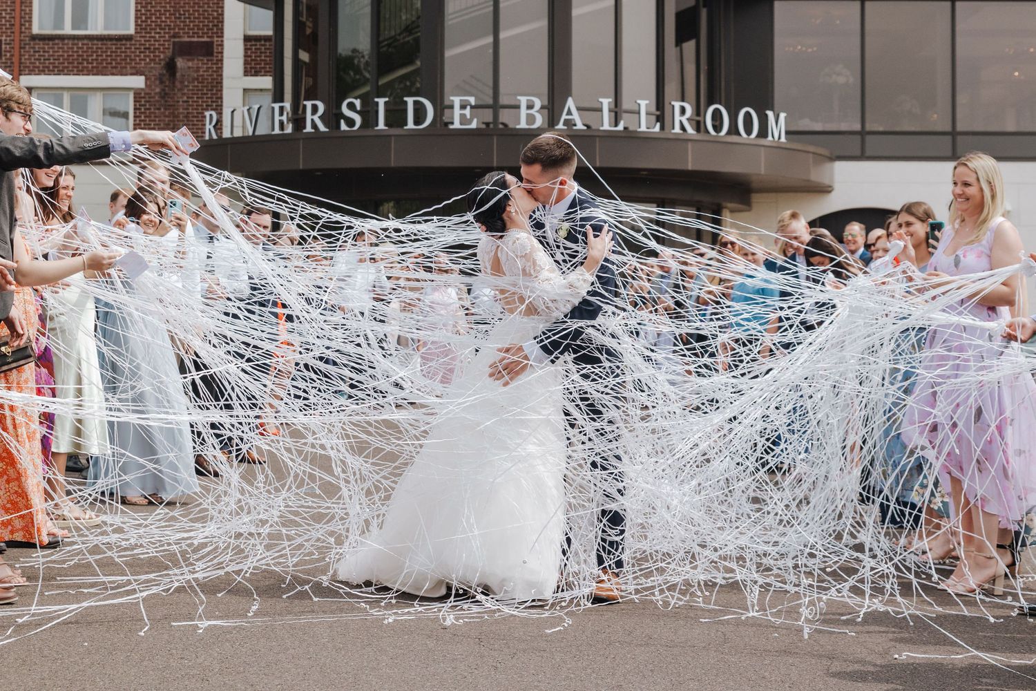 Wedding guests create a tunnel of white streamers for the newlyweds to run through during their celebration exit.