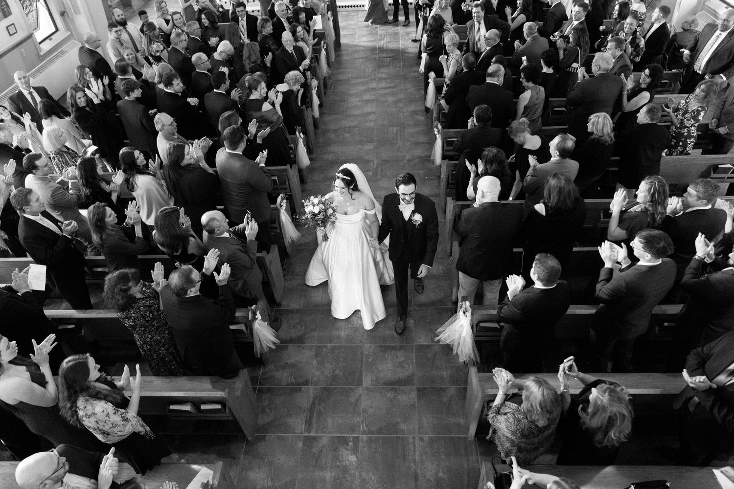 A large indoor wedding ceremony with guests seated in rows while a couple exchanges vows at the altar.