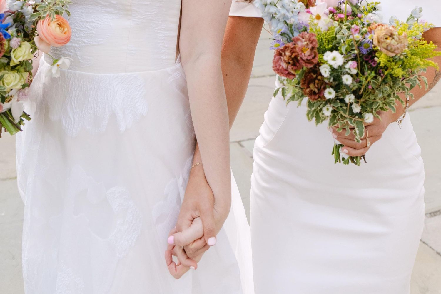 A close-up view of a bridal bouquet with pink and white flowers against a white dress background.
