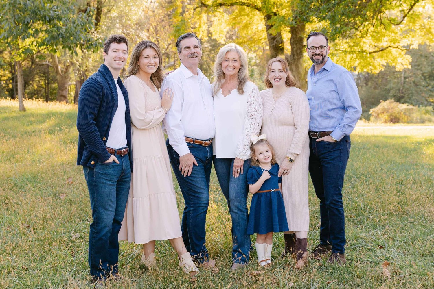 A group wearing coordinated navy and blush outfits poses together in a sunlit autumn field.
