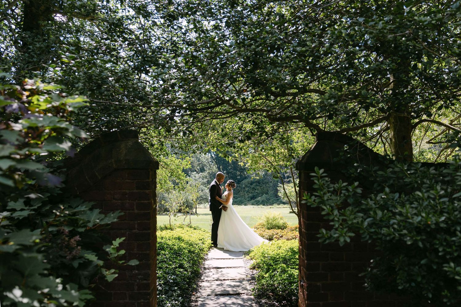 A romantic garden archway framed by brick walls and lush greenery creates an enchanting outdoor scene.