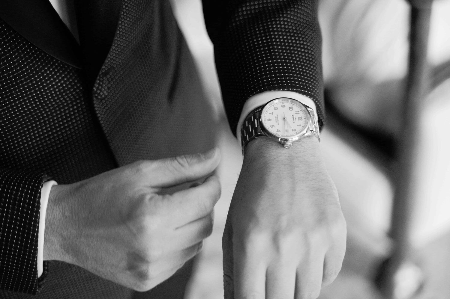 A black and white photo showing a person's hands buttoning up a formal dress shirt sleeve.