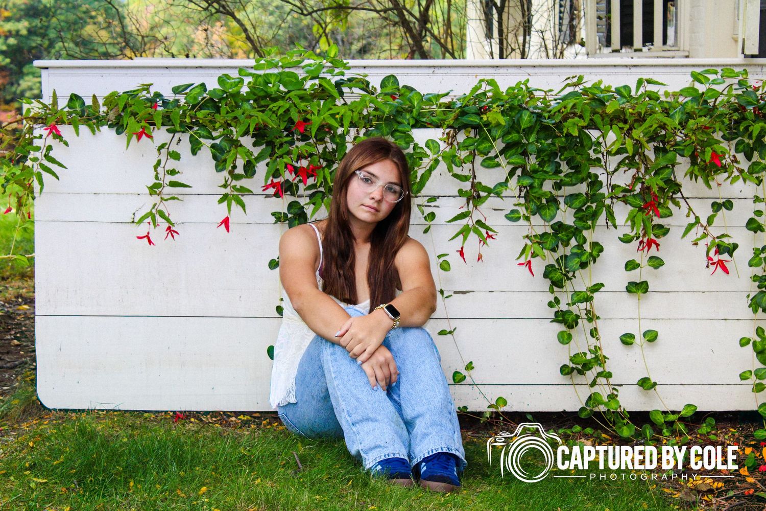 This is a picture of a girl sitting in front of a fence with vines