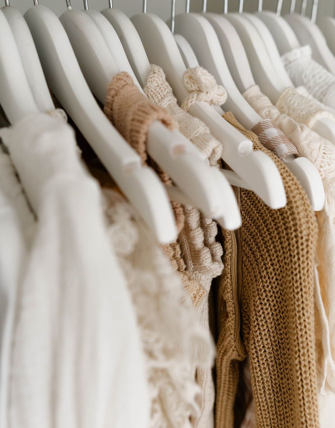 A collection of white and cream colored clothing hanging neatly on white hangers in a closet.