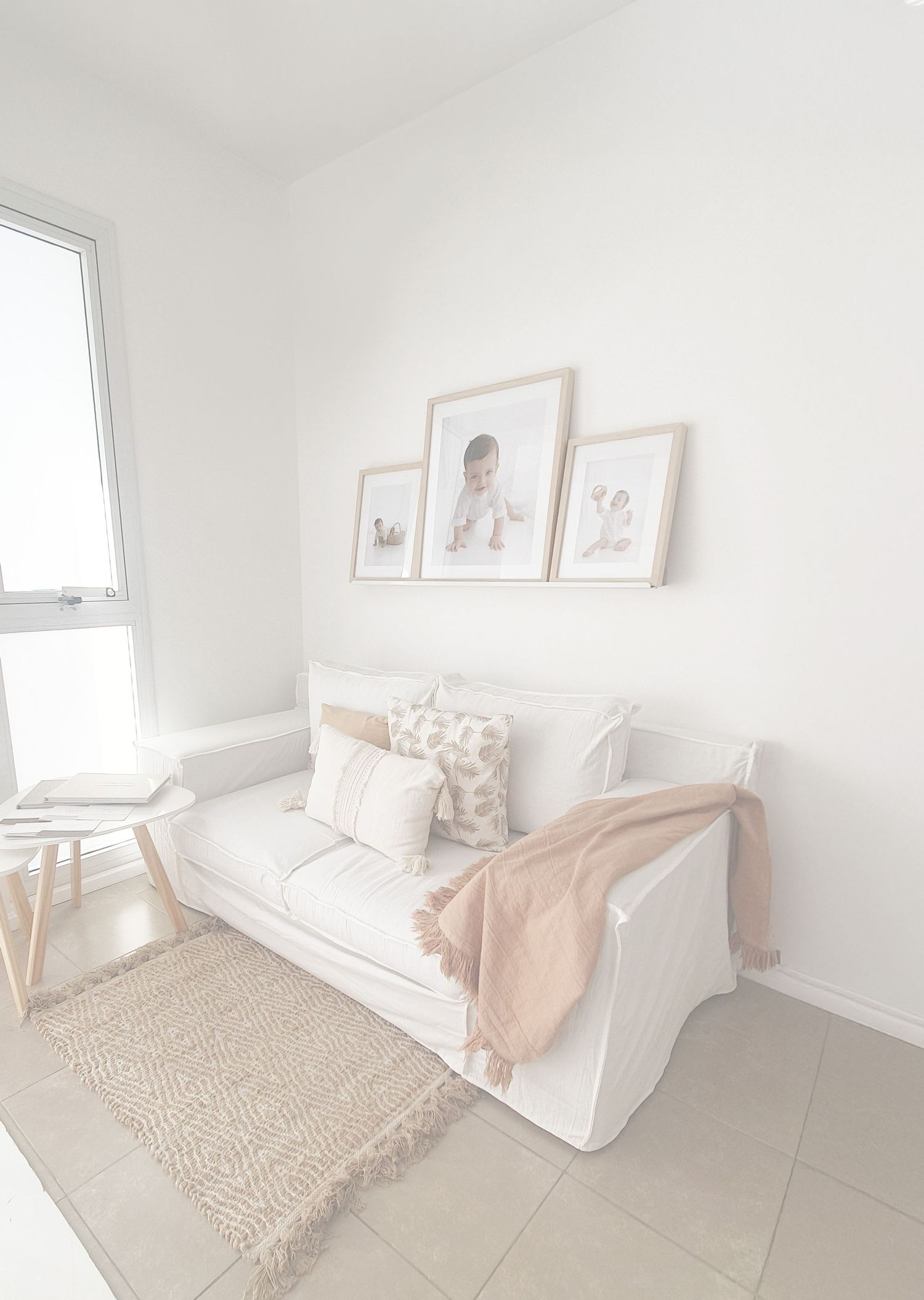 Minimalist white room with daybed, framed artwork, jute rug and soft blush accents creating a serene aesthetic.