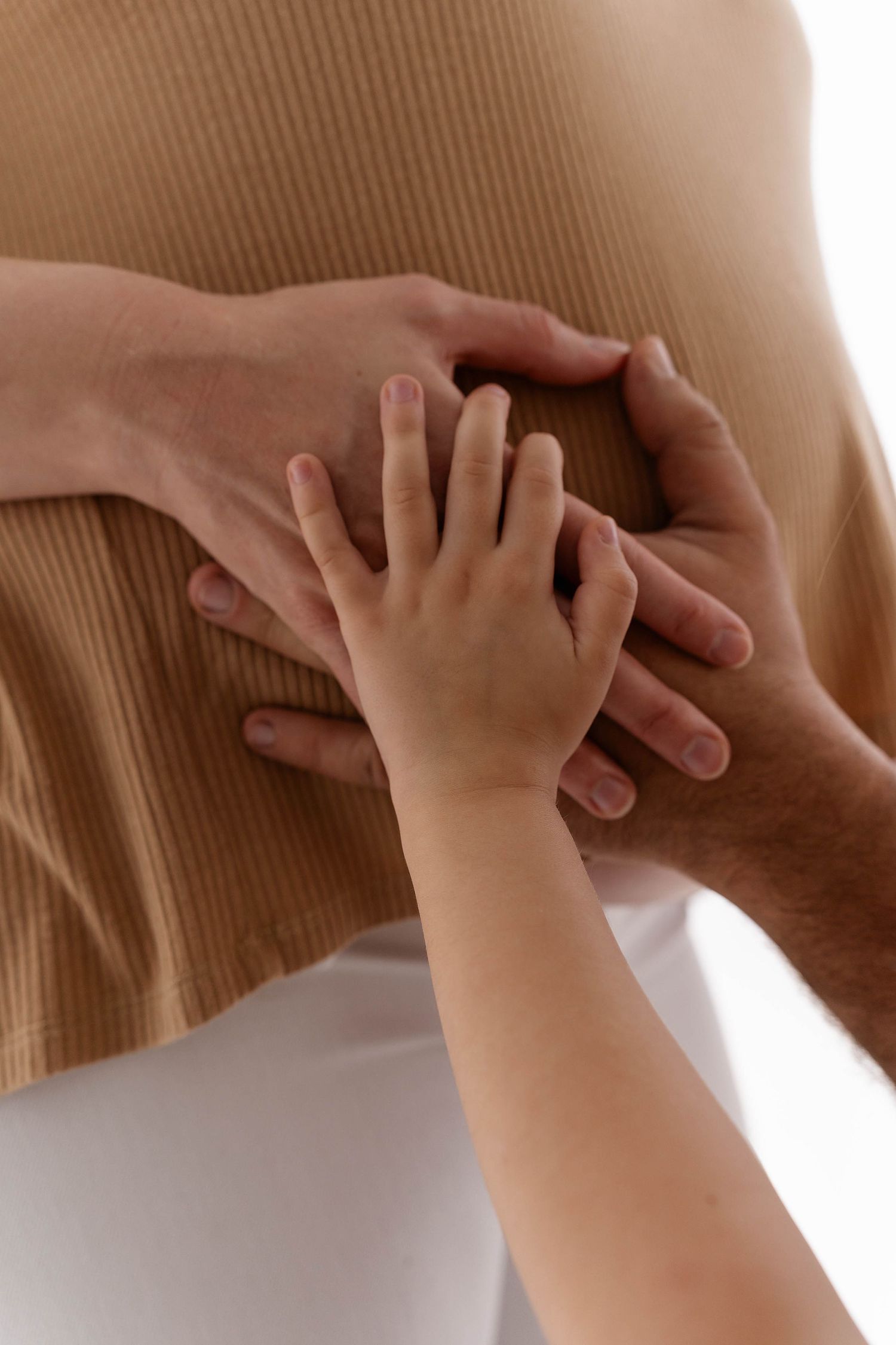 Close-up of adult and child hands touching against a brown background.