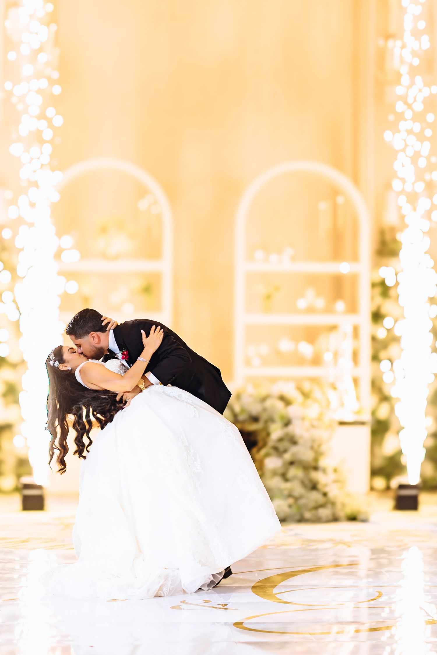 A bride and groom share a romantic dip while dancing on an illuminated white dance floor at their wedding reception.
