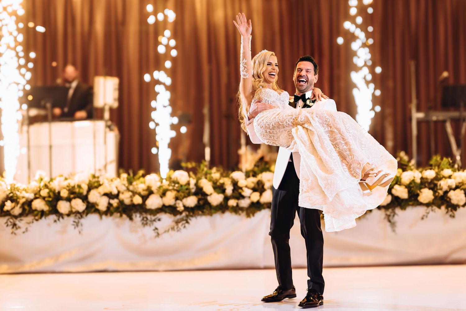 A couple shares their first dance at a wedding reception with romantic string lights and floral decor in the background.