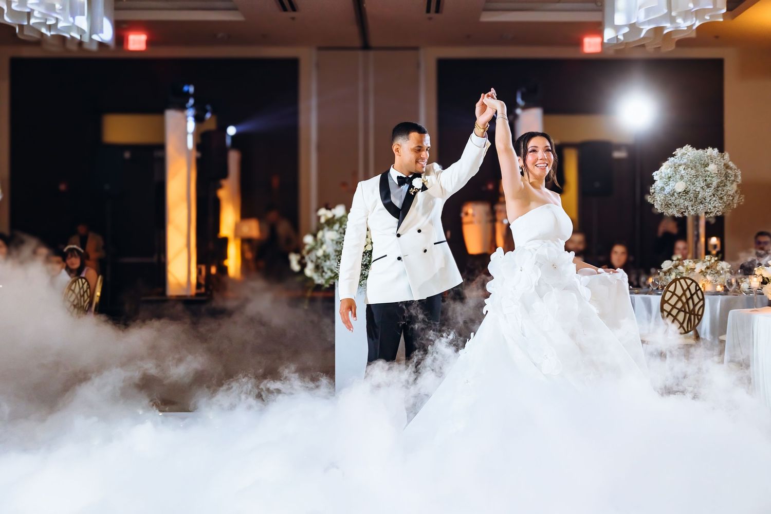 Bride and groom share first dance surrounded by dramatic fog on elegant wedding reception dance floor.