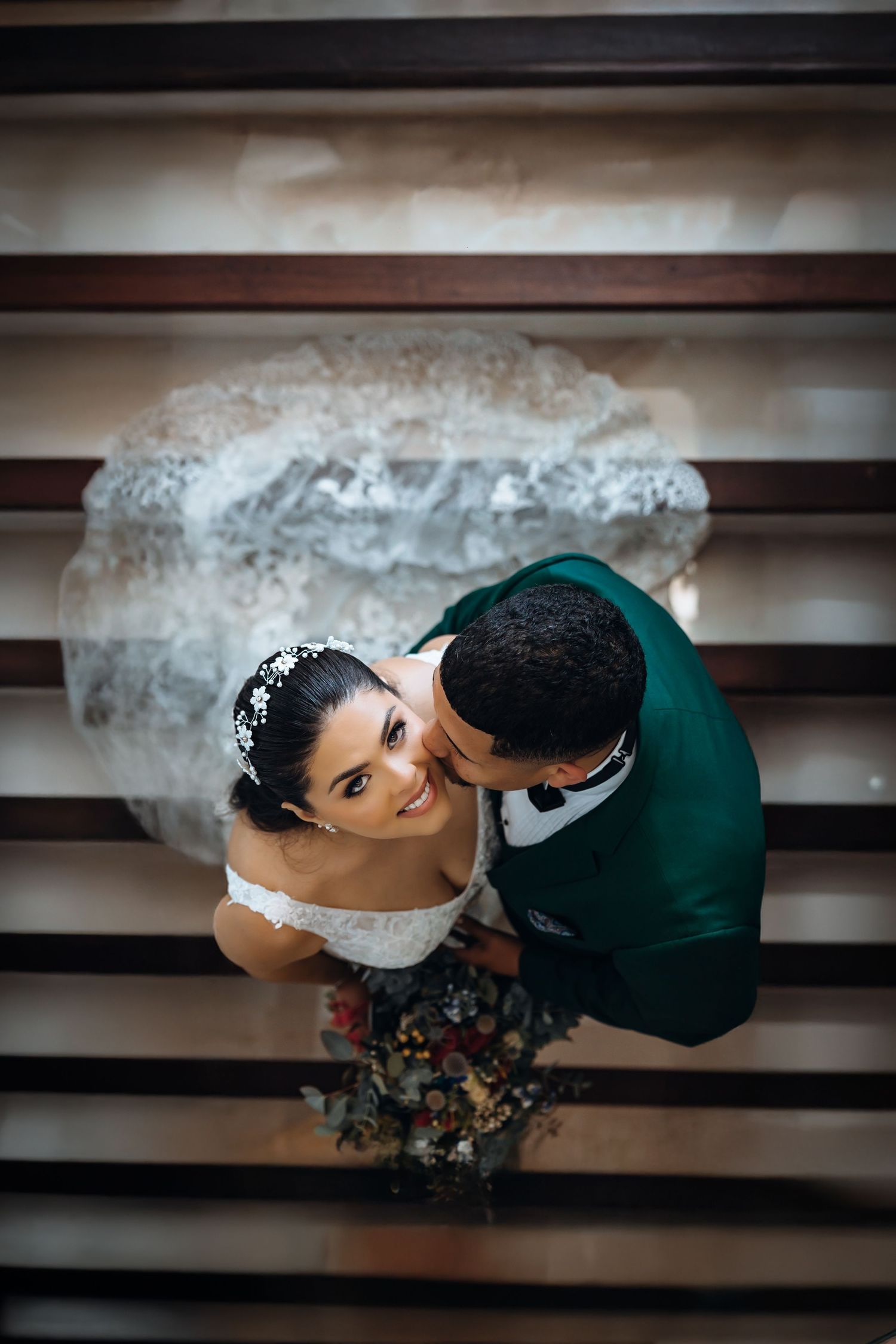Aerial view of bride and groom in romantic wedding photo shoot on wooden staircase.