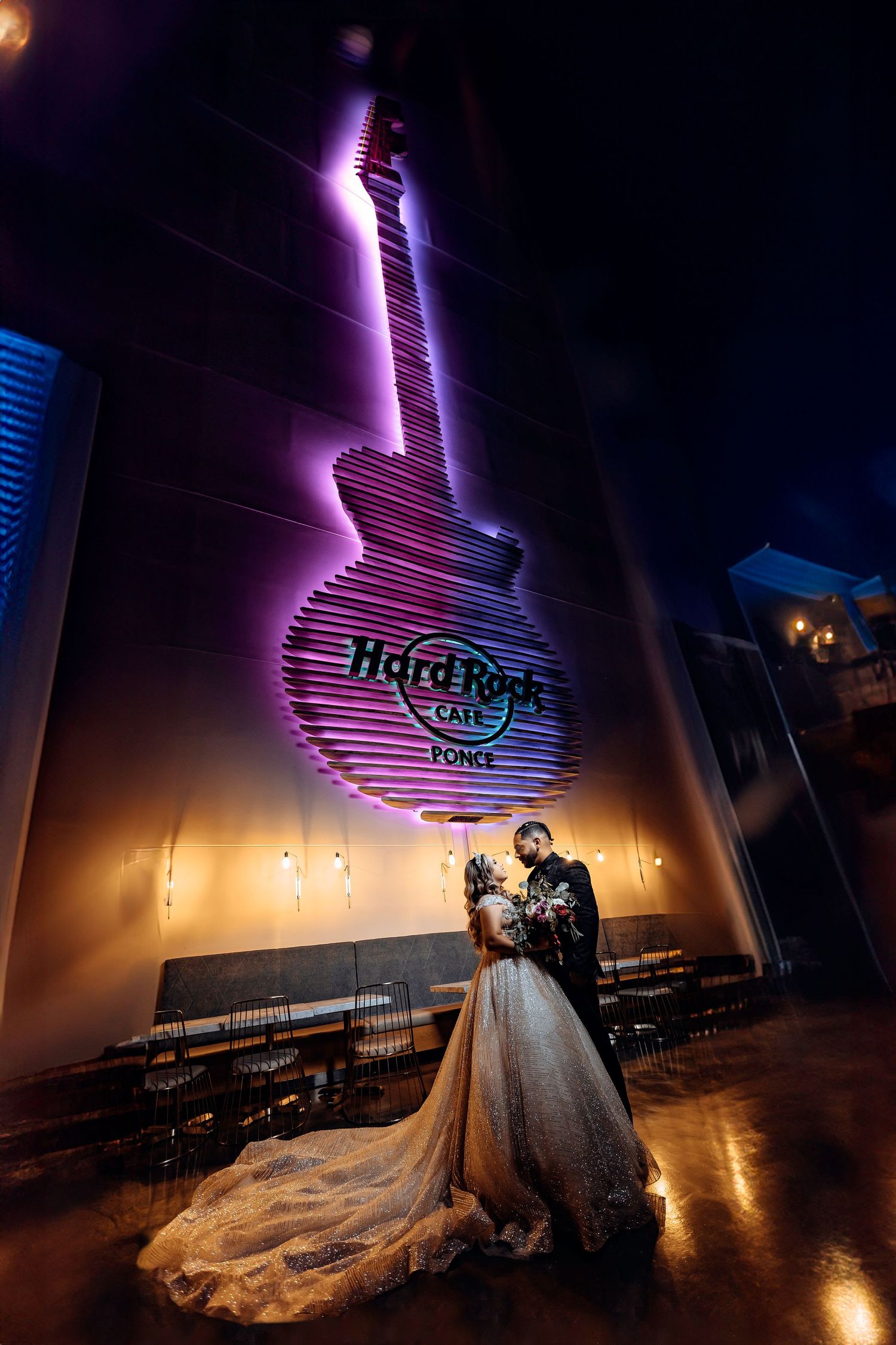 A couple shares a romantic moment under a glowing purple Hard Rock Cafe guitar sign at night.
