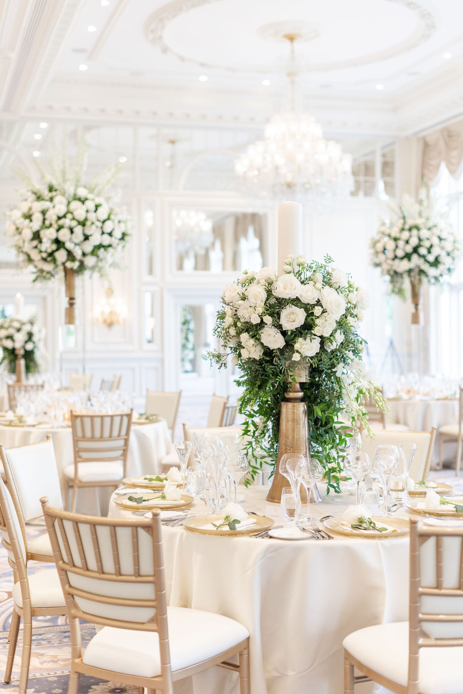 Elegant white wedding reception setup with tall floral centerpieces and crystal chandeliers in a luxurious ballroom. Trump Turnberry.