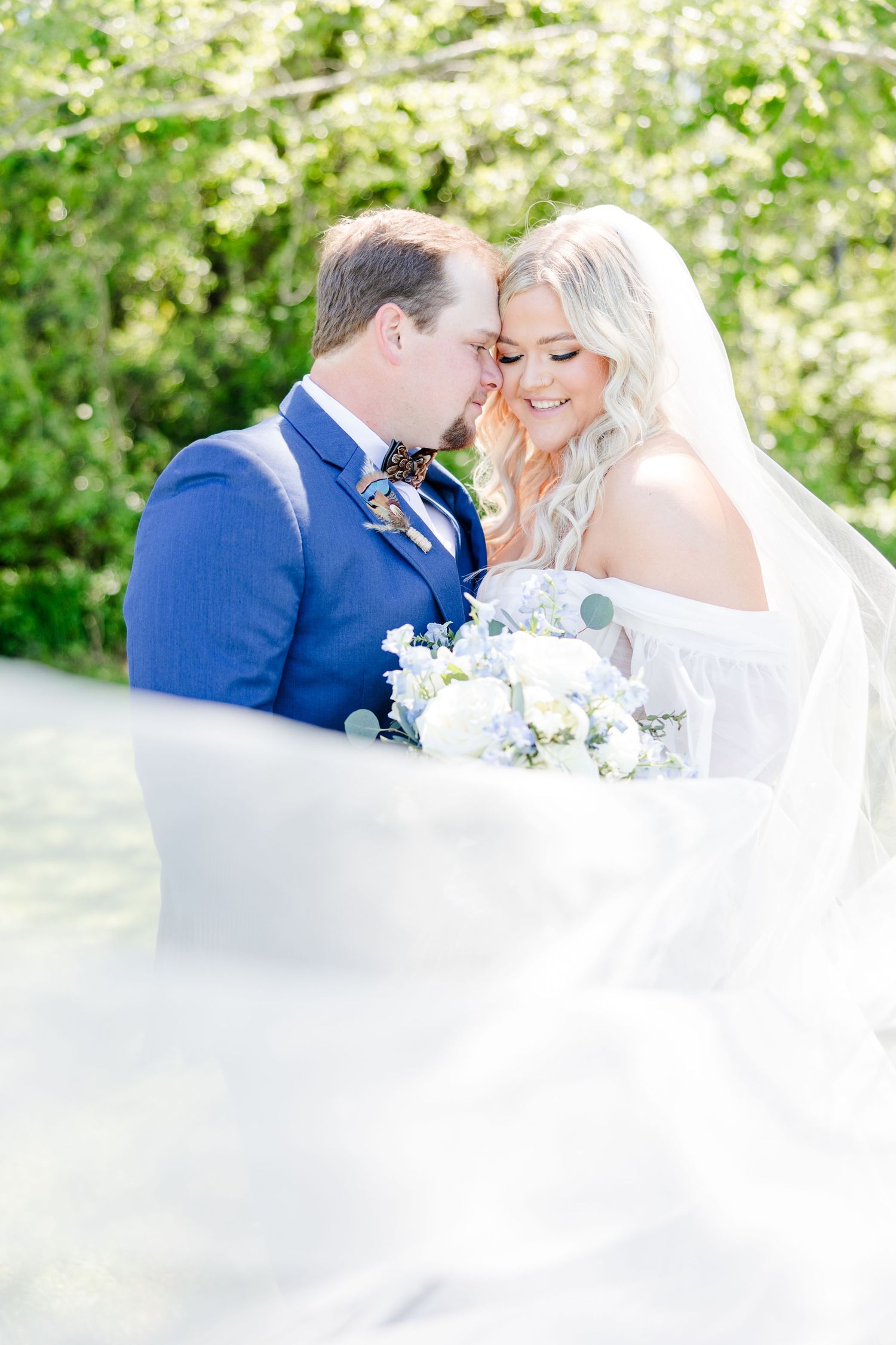 Romantic wedding couple shares intimate moment in a sunlit garden with white floral bouquet.