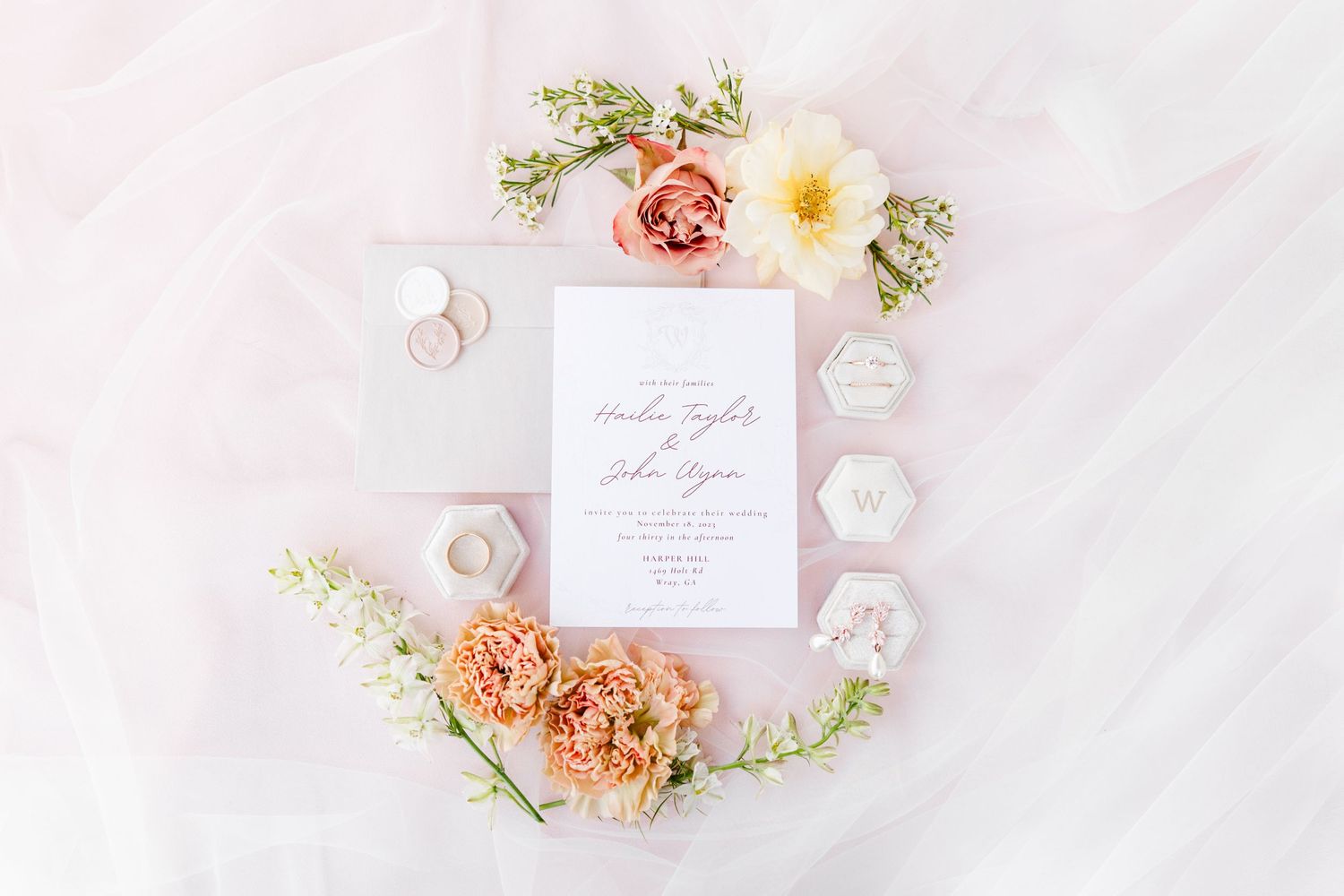 Wedding invitation with peach roses and hexagonal details on white fabric.