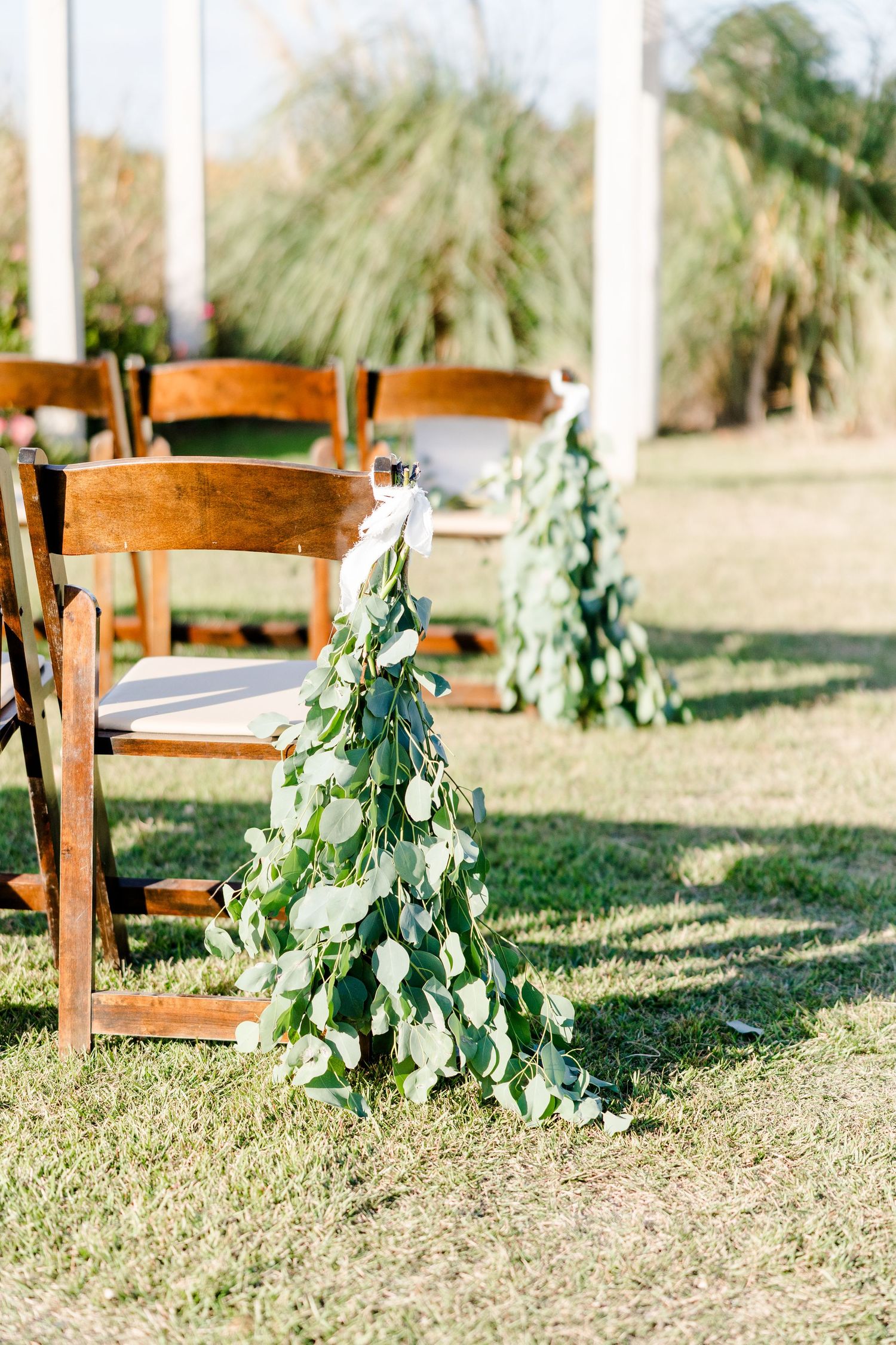 Wooden chairs decorated with cascading greenery garlands at an outdoor wedding ceremony.