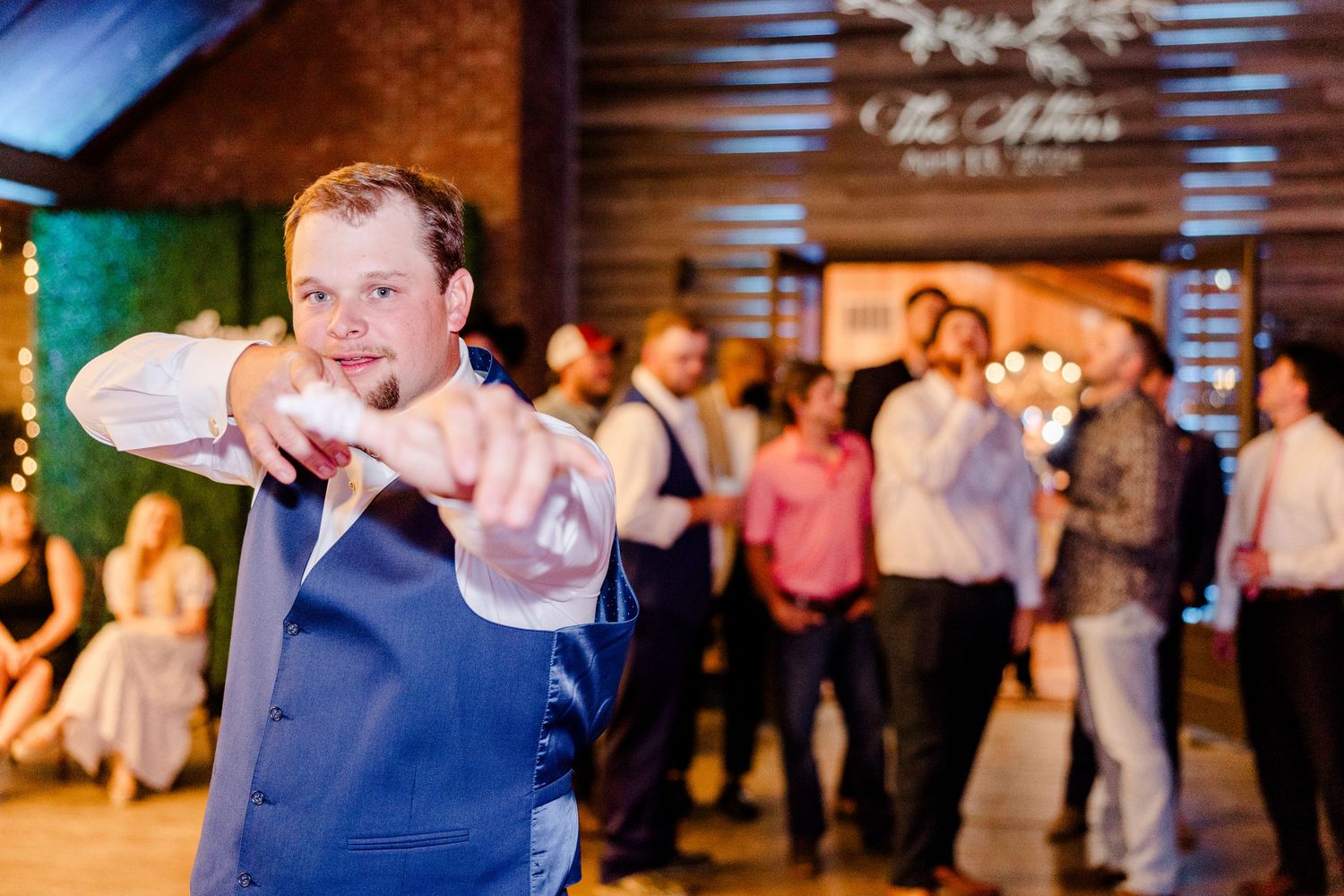 Wedding guests dance and celebrate joyfully at an indoor reception venue with warm lighting.