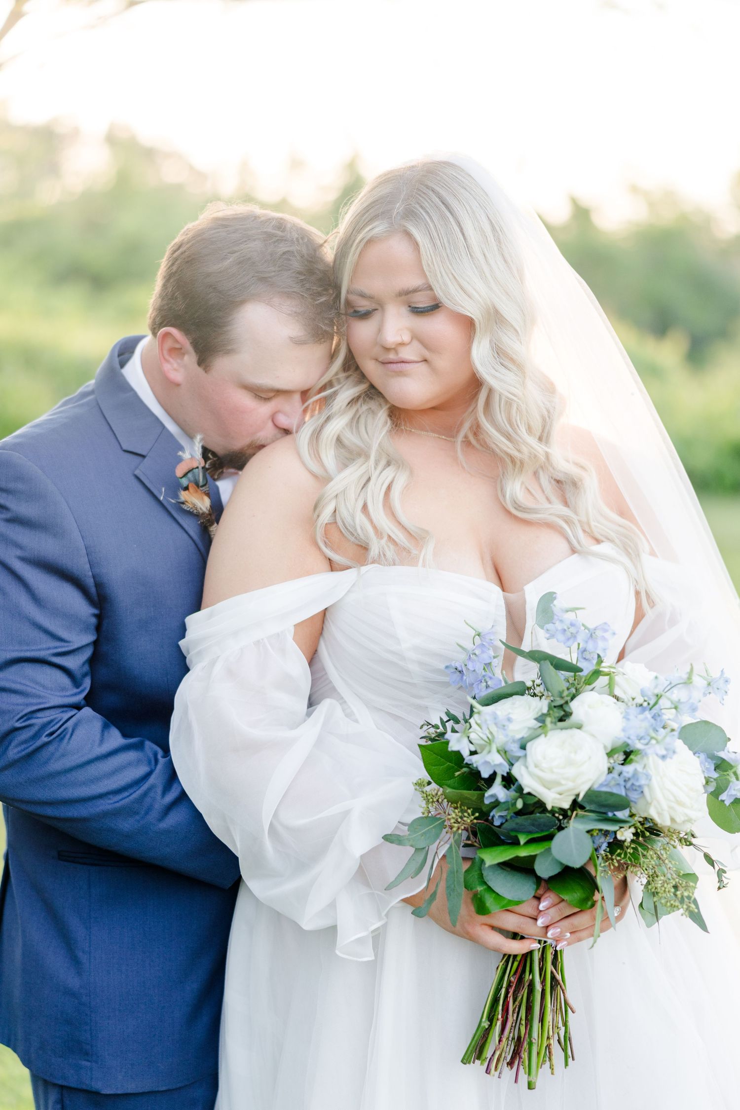 A tender wedding moment captured in golden sunlight with a beautiful white and blue bouquet.