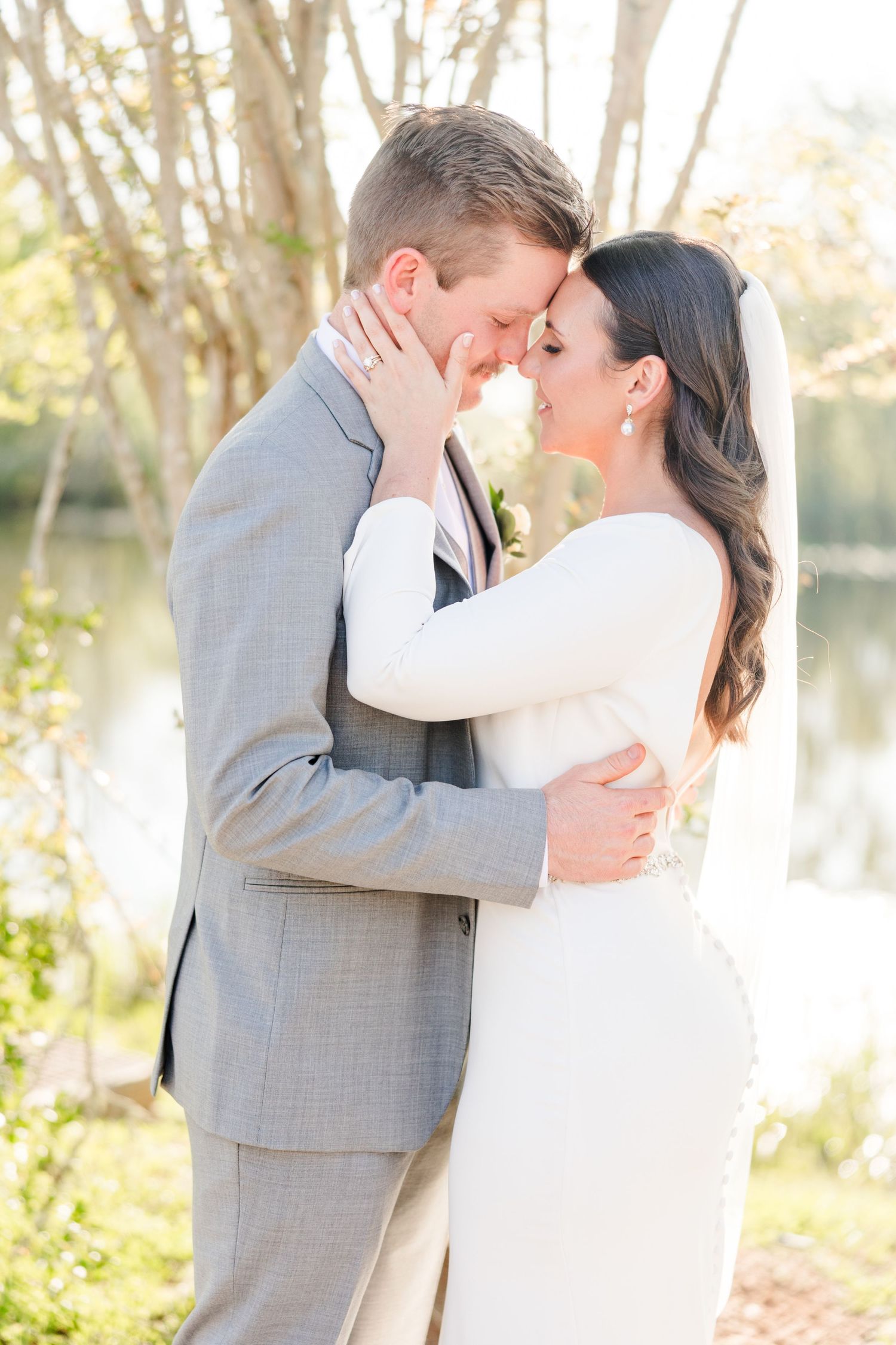 Romantic wedding portraits by lake with sunlight filtering through trees.
