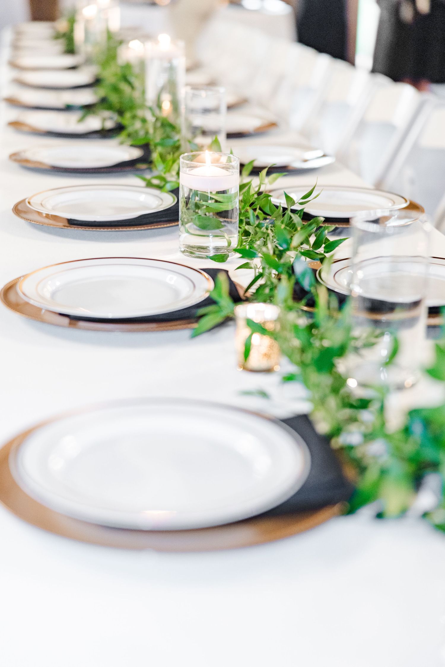 Elegant table setting with white plates, greenery garland runner, and glass candle holders.