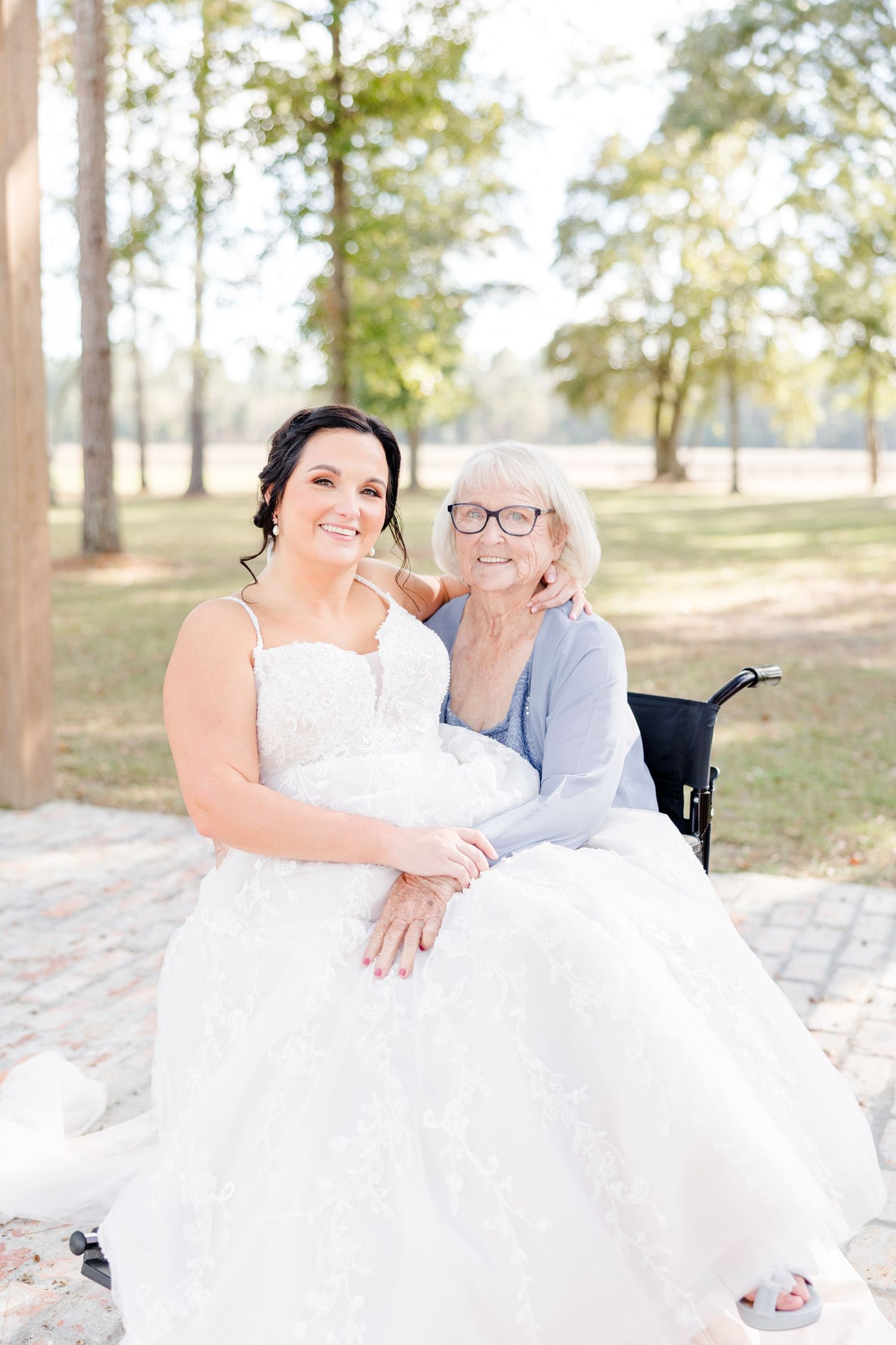 A romantic outdoor wedding photoshoot with a couple lounging on elegant white furniture under trees.