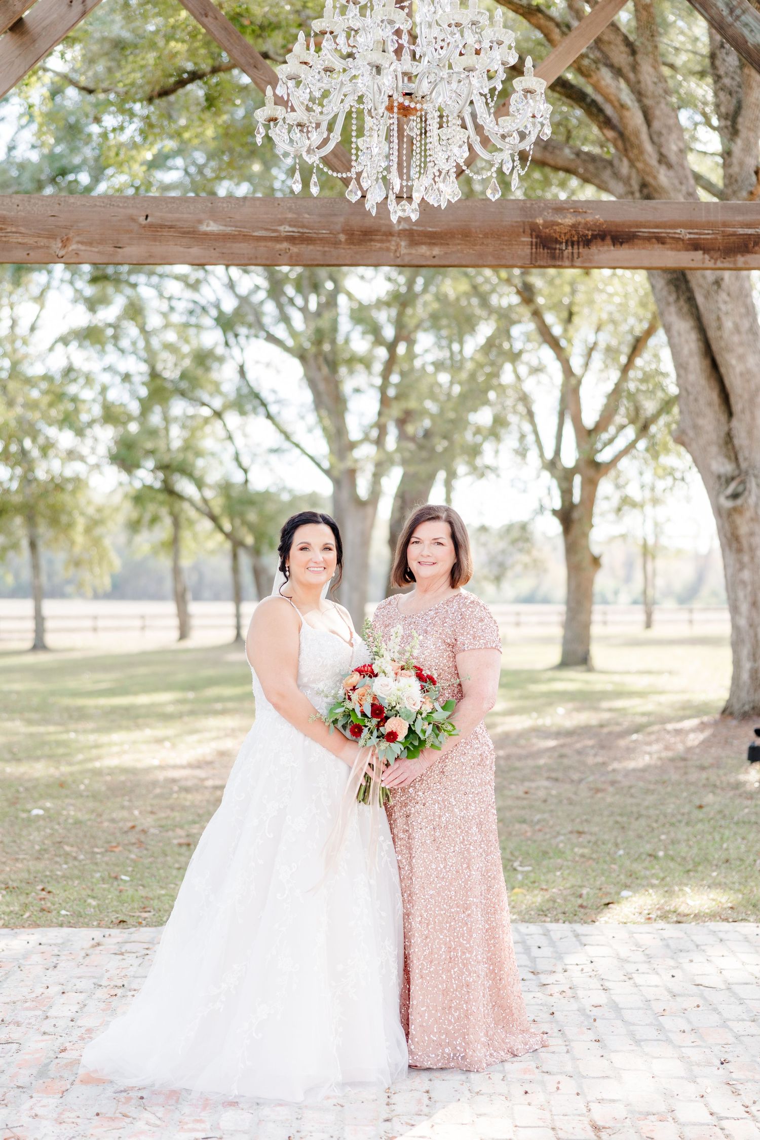 Wedding party members in blush pink dresses pose with bouquets in a sunlit outdoor setting.
