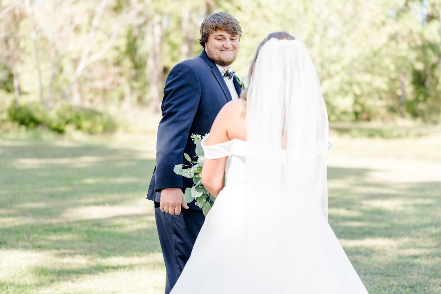 Bride in white gown and groom in navy suit pose together outdoors.