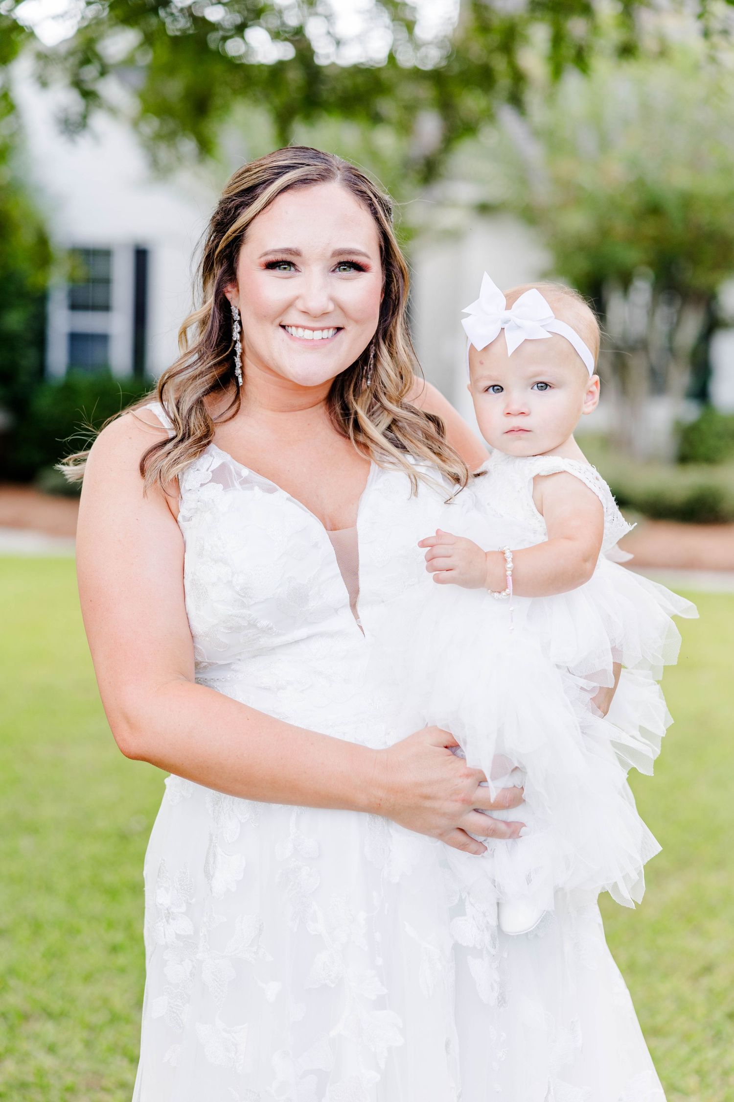 Mother and baby in matching white dresses posing outdoors on a sunny day.