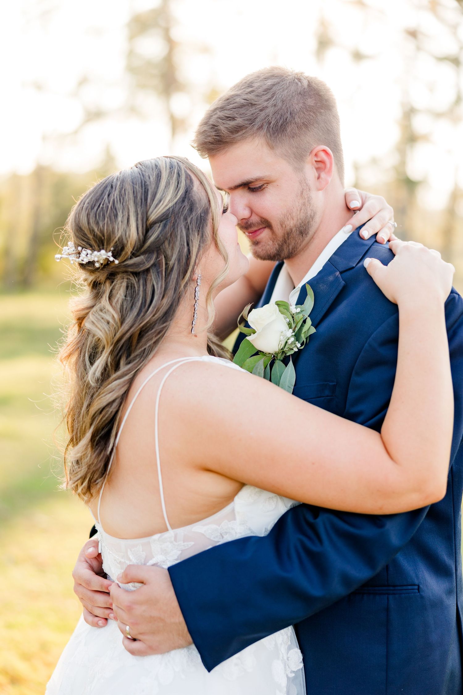 An intimate wedding embrace captured in soft golden sunlight with pine trees in the background.