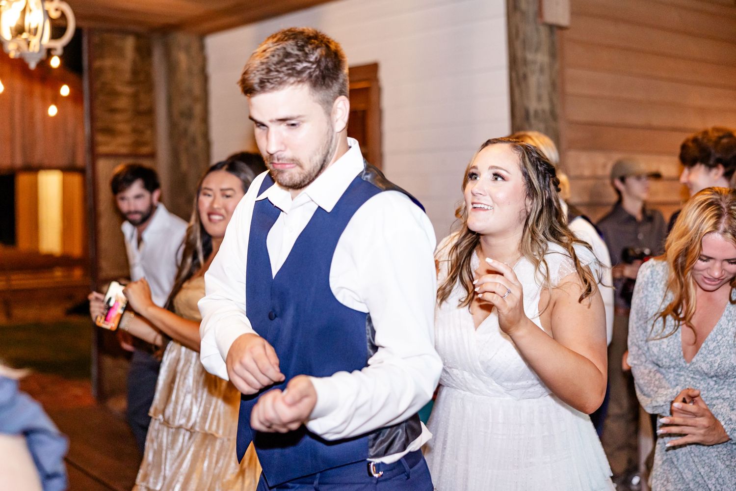 Wedding reception guests dancing and celebrating in rustic wooden venue.