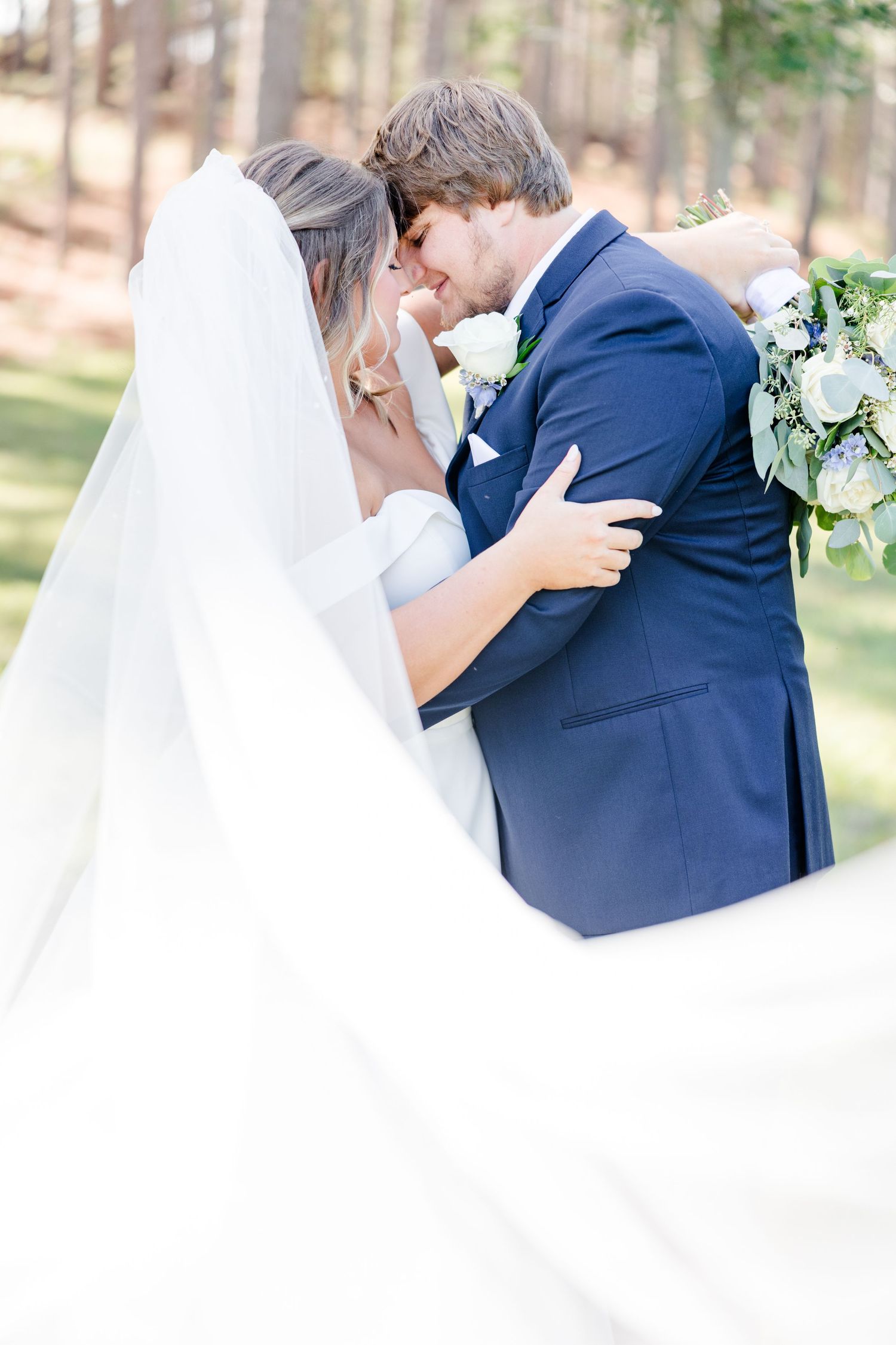Intimate wedding portrait of couple sharing a tender moment in an outdoor woodland setting.