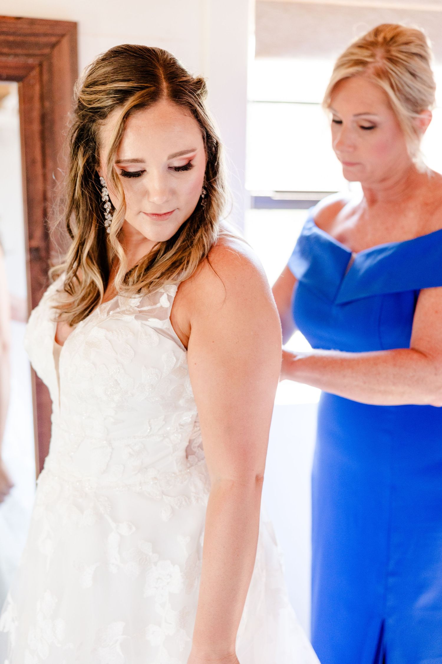 A bride in a lace wedding gown getting final adjustments to her dress.