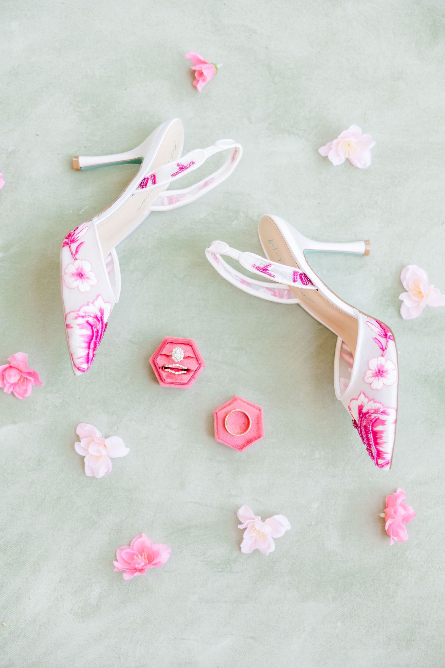 White floral embroidered bridal heels with pink cherry blossoms, ring box, and scattered pink flowers on mint background.