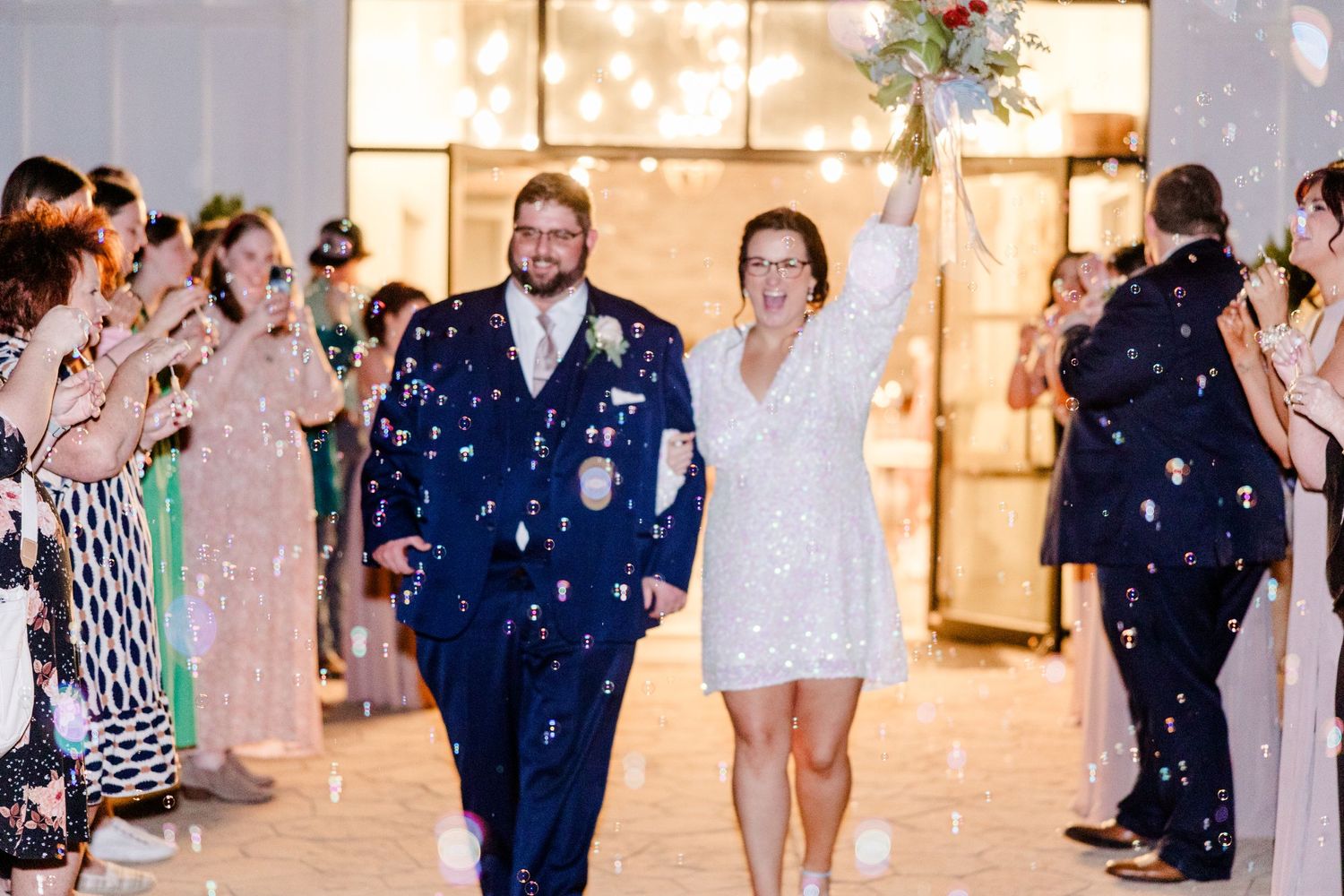 Wedding celebration with confetti being thrown at a couple exiting a brightly lit venue.