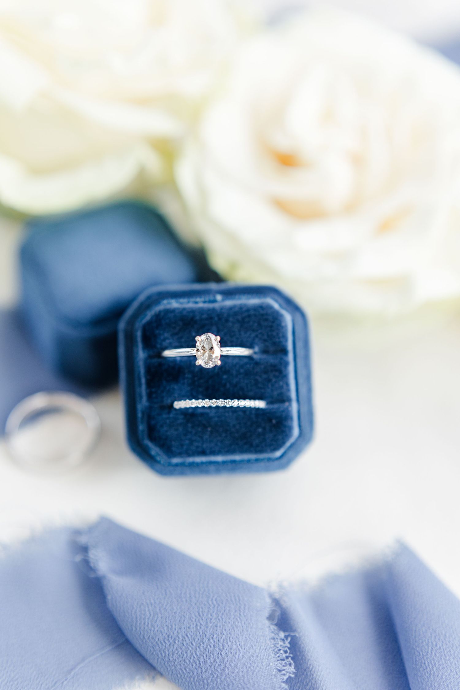 Diamond engagement ring and wedding band in navy blue velvet ring box with white roses.