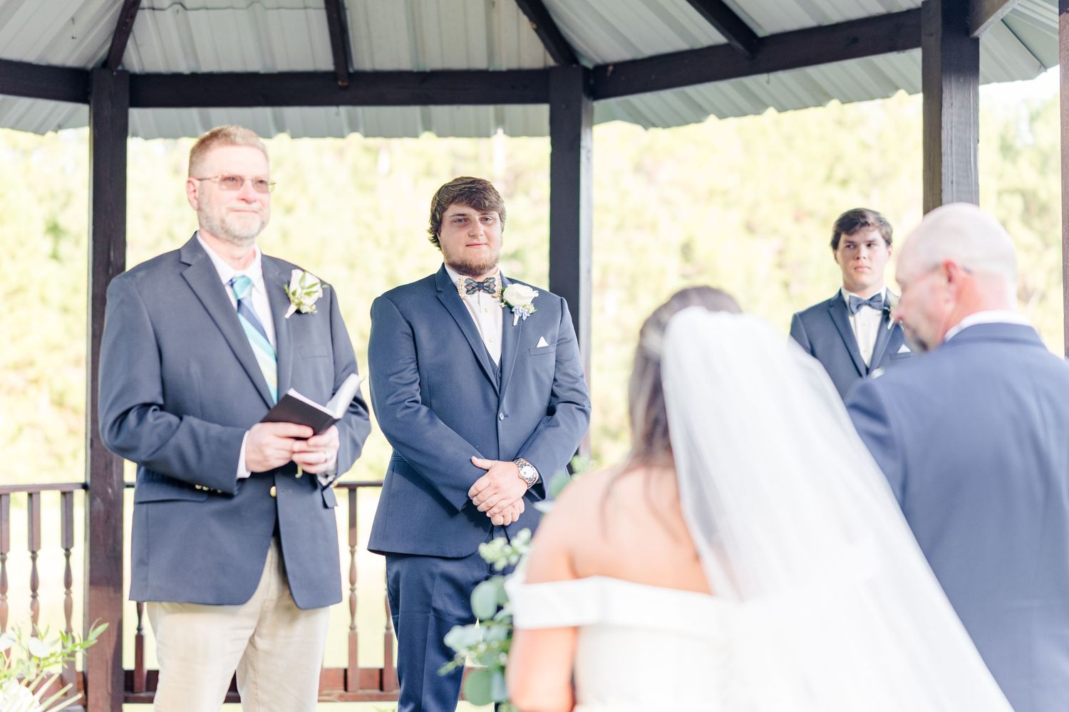 Wedding party gathers under covered pavilion during outdoor celebration.