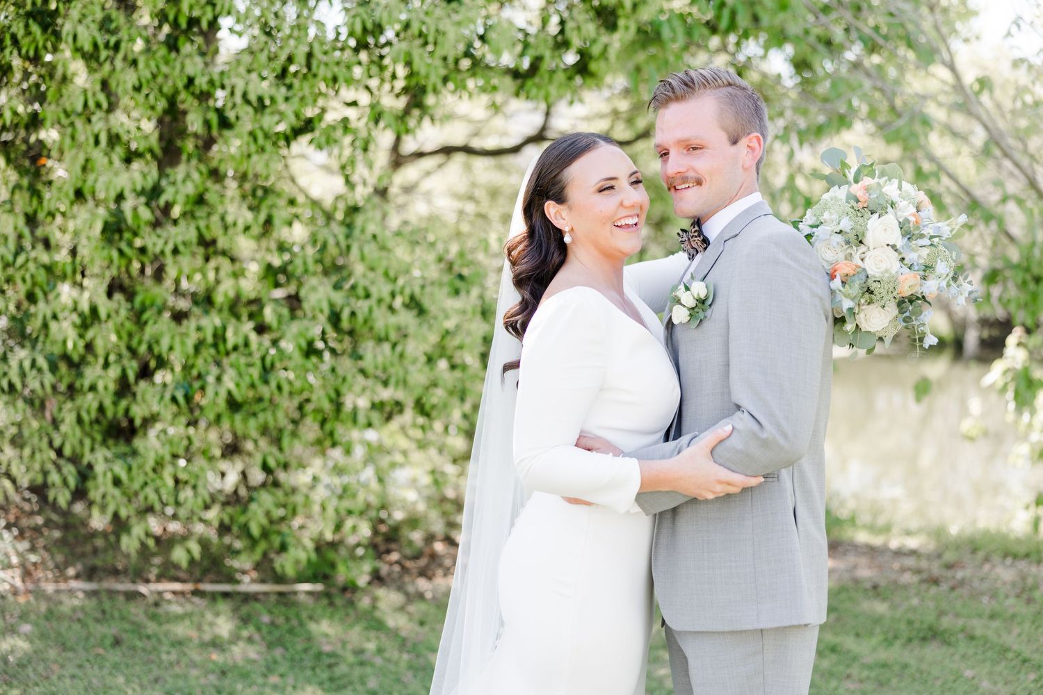 Wedding couple poses together in sunlit garden with white flowers and greenery.
