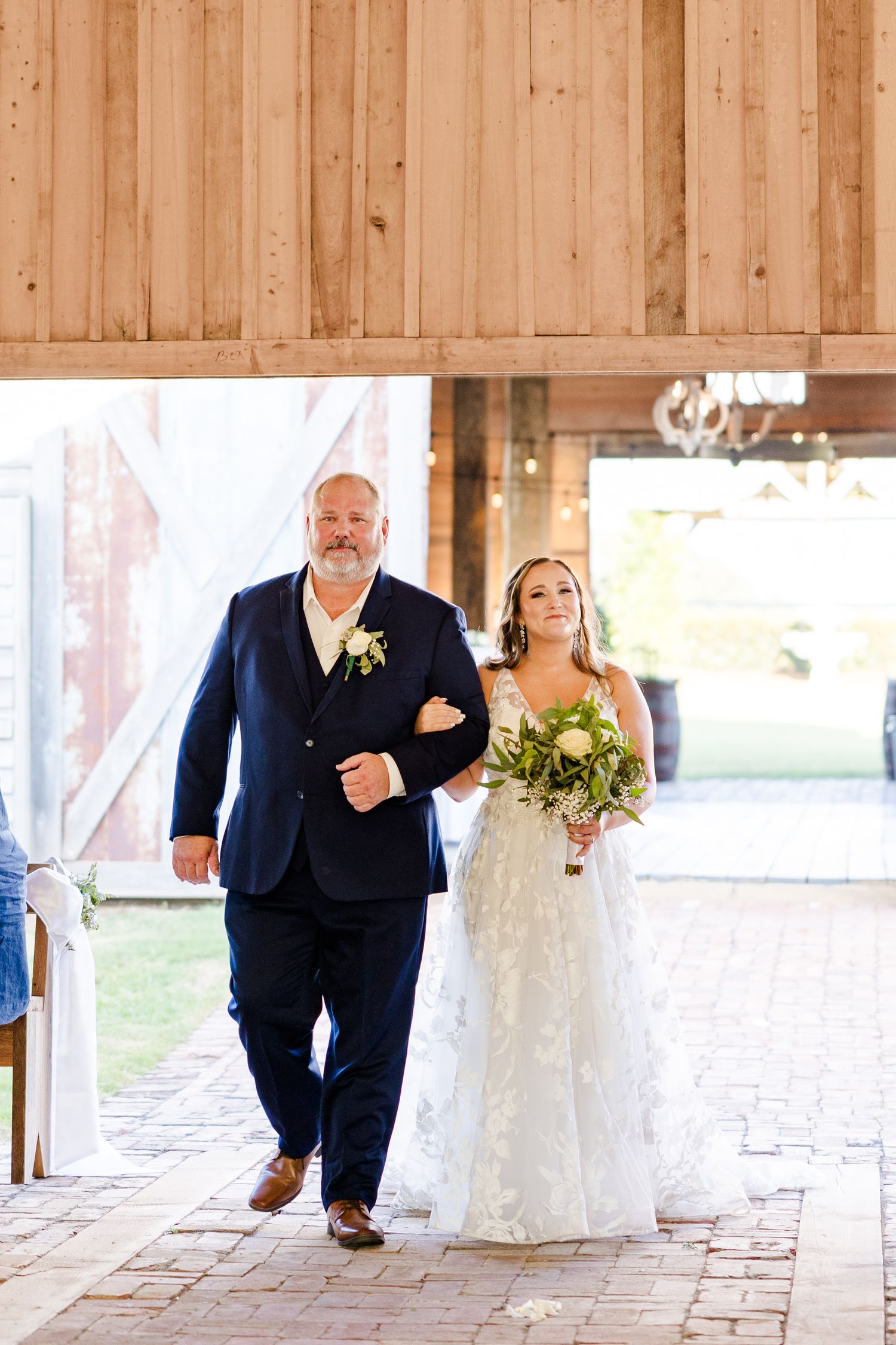 A wedding party walks through a rustic wooden barn venue with natural lighting.