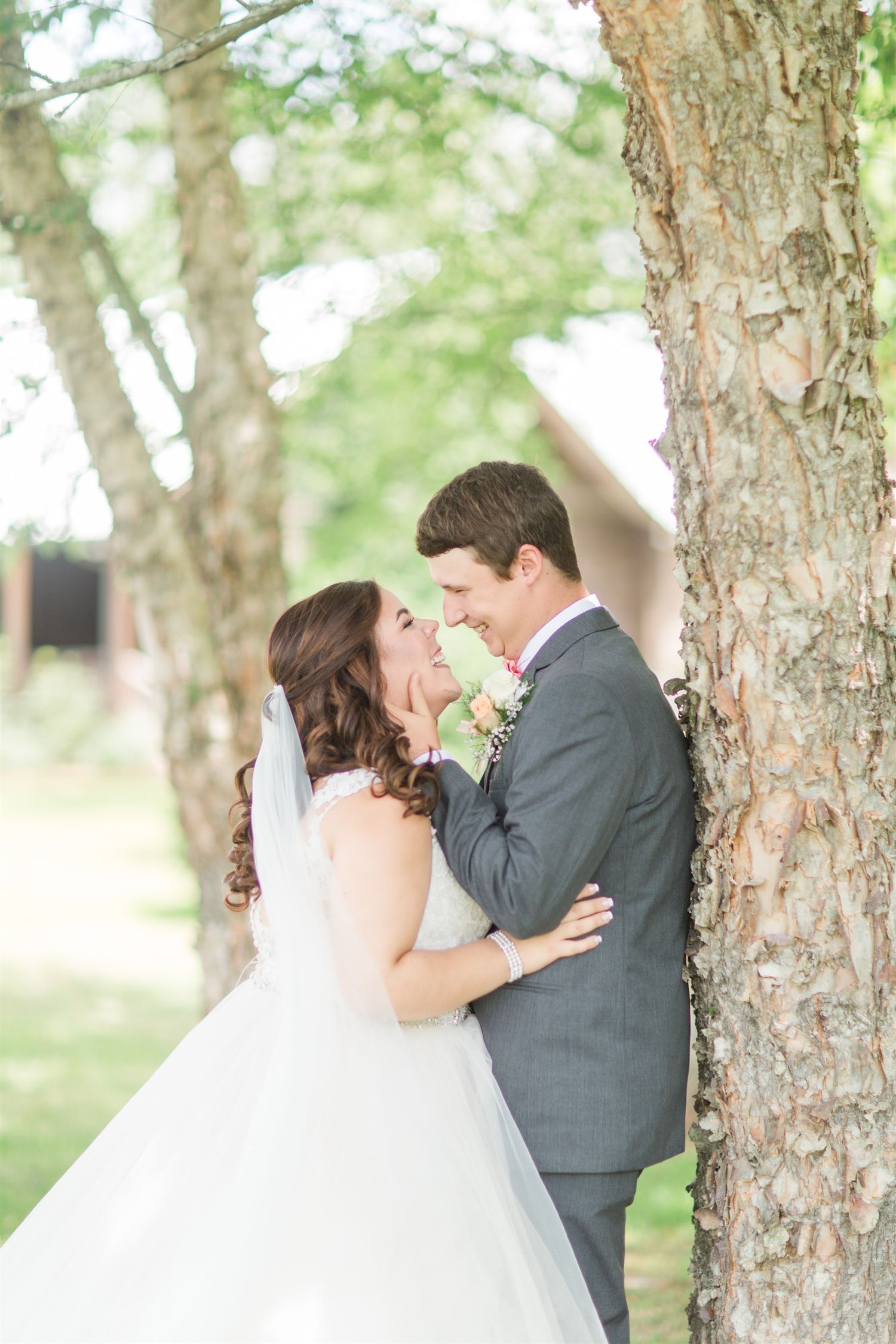 Bride and groom share a romantic moment leaning against a tree in an outdoor wedding setting.