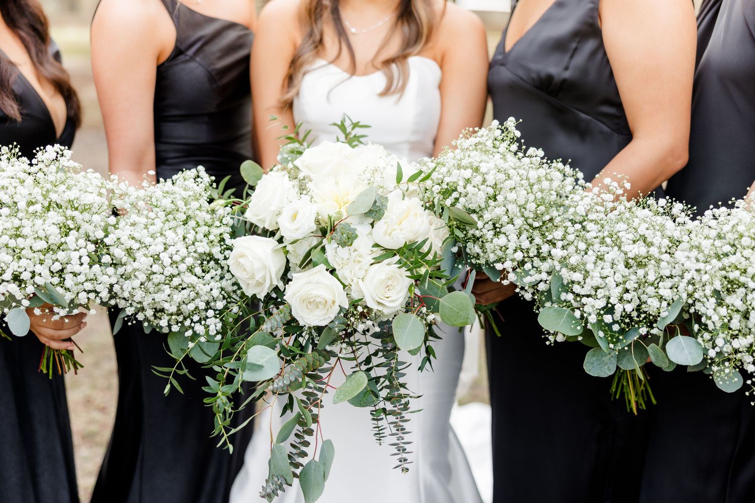 Row of white rose and baby's breath bouquets held by wedding party members.