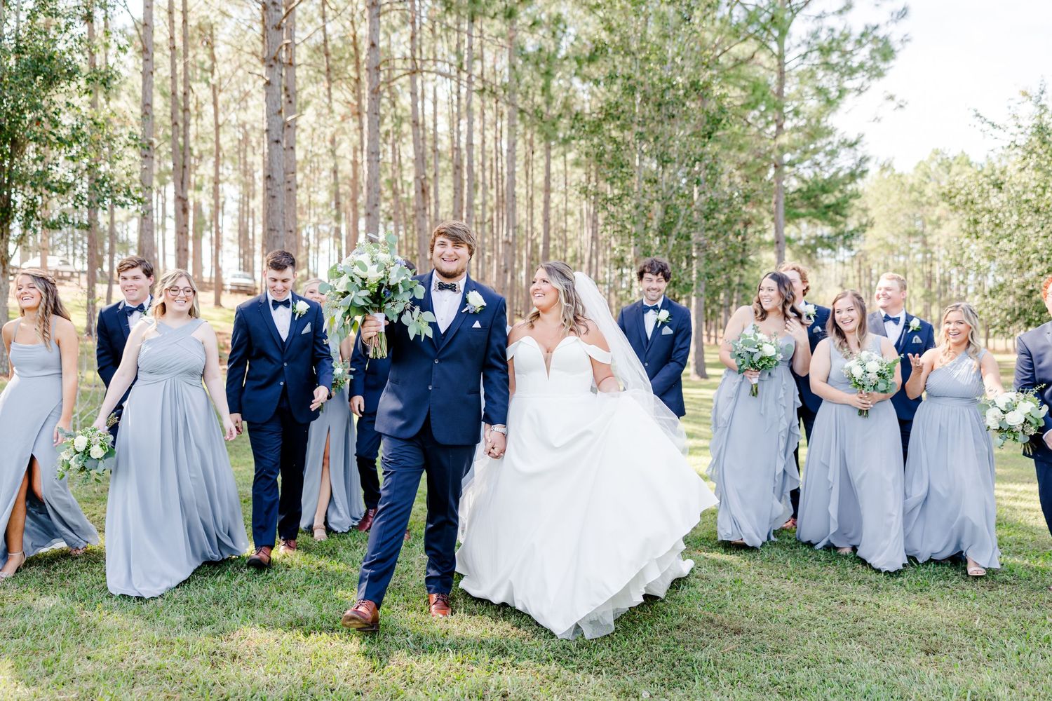 Large wedding party poses for group photos in an outdoor forest setting.