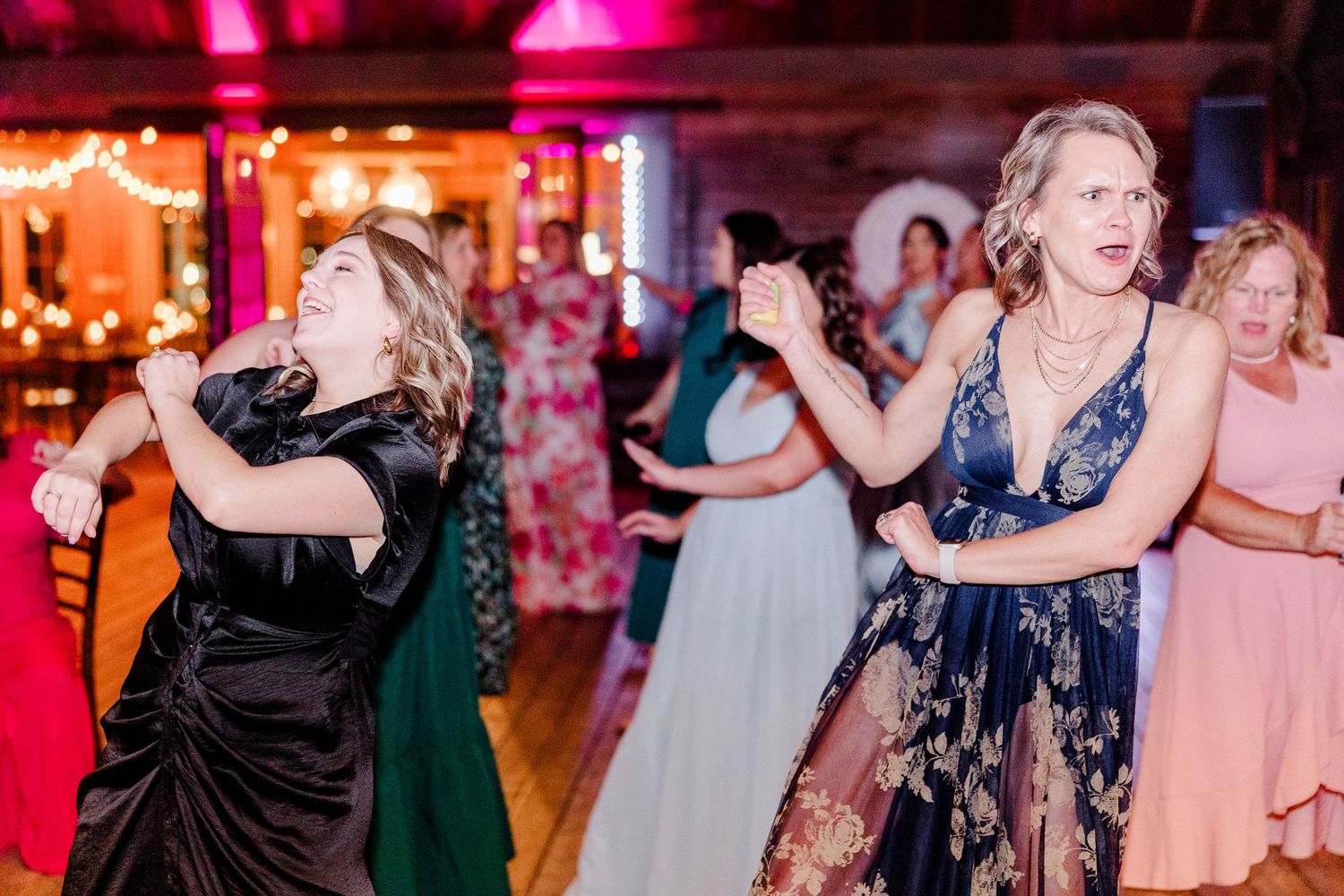 Wedding guests dancing under colorful pink and red lighting at evening reception.