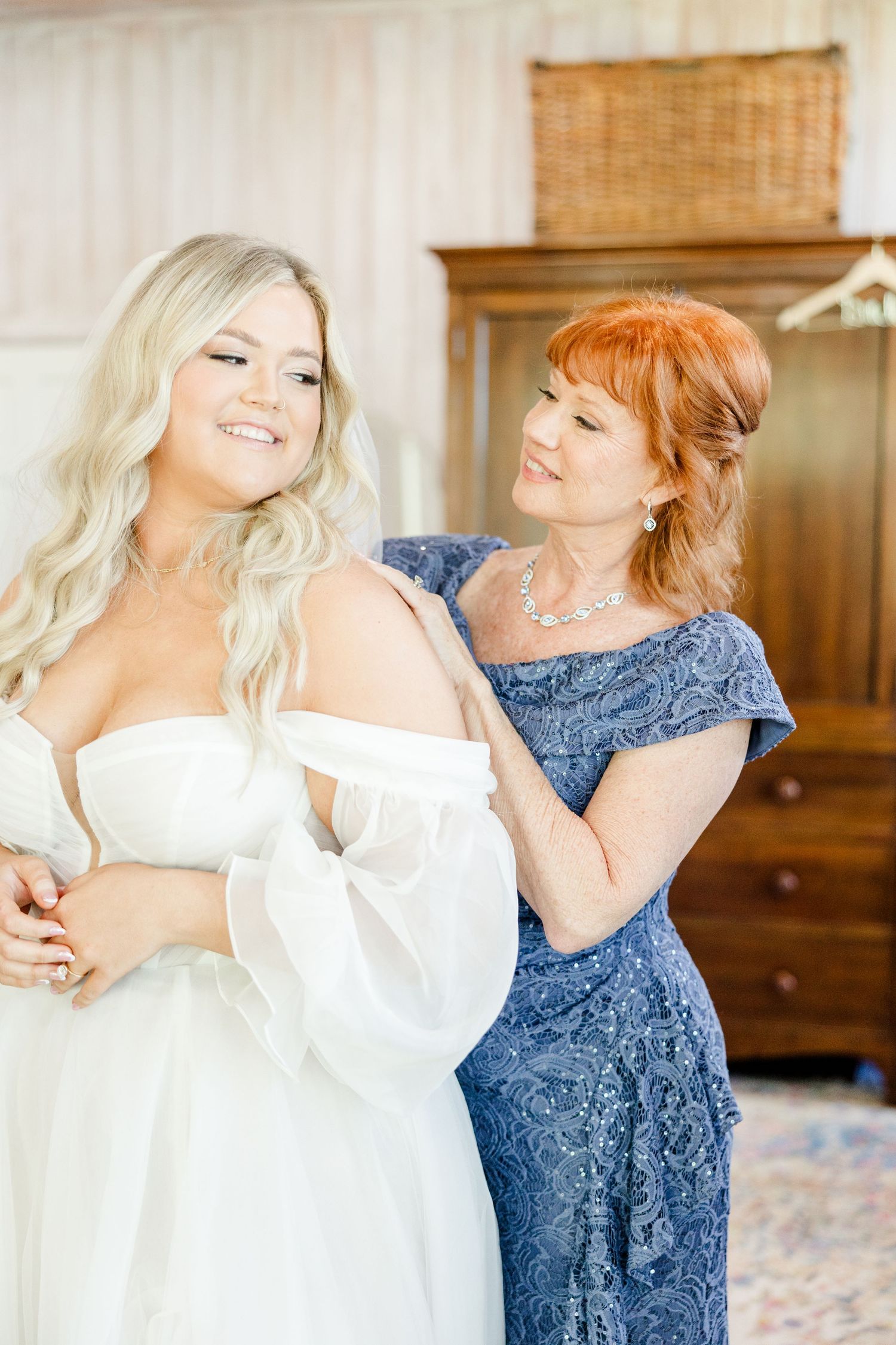 Getting ready scene with bride in white robe and helper in navy blue dress.