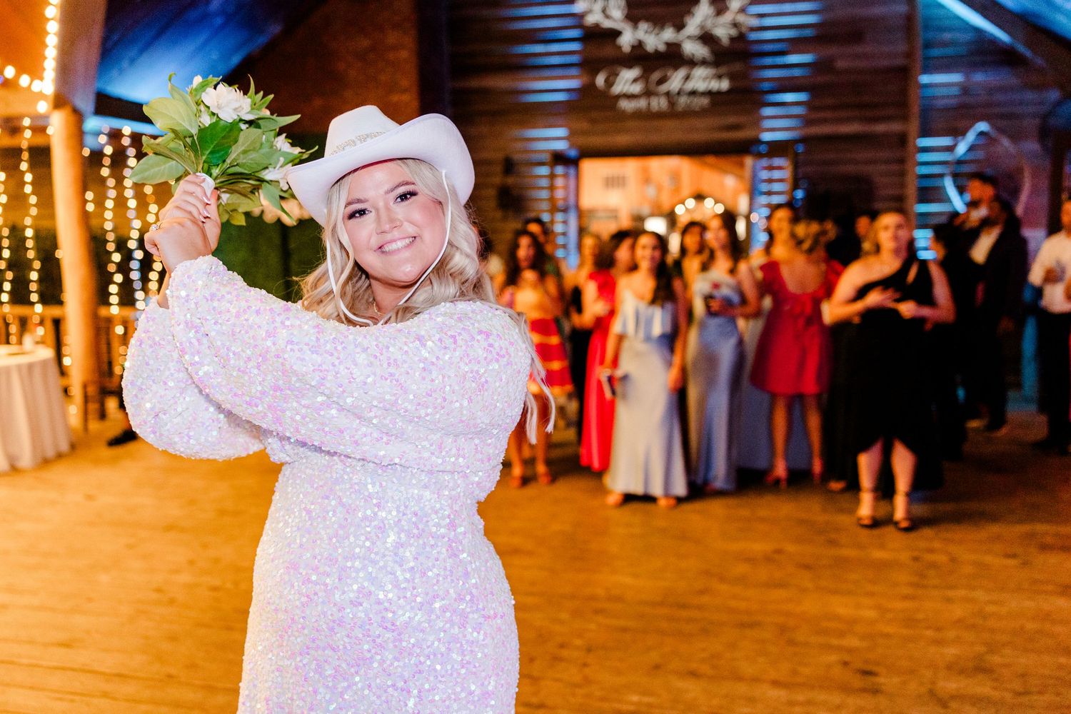 Wedding celebration dance floor with string lights and rustic wooden beams overhead.
