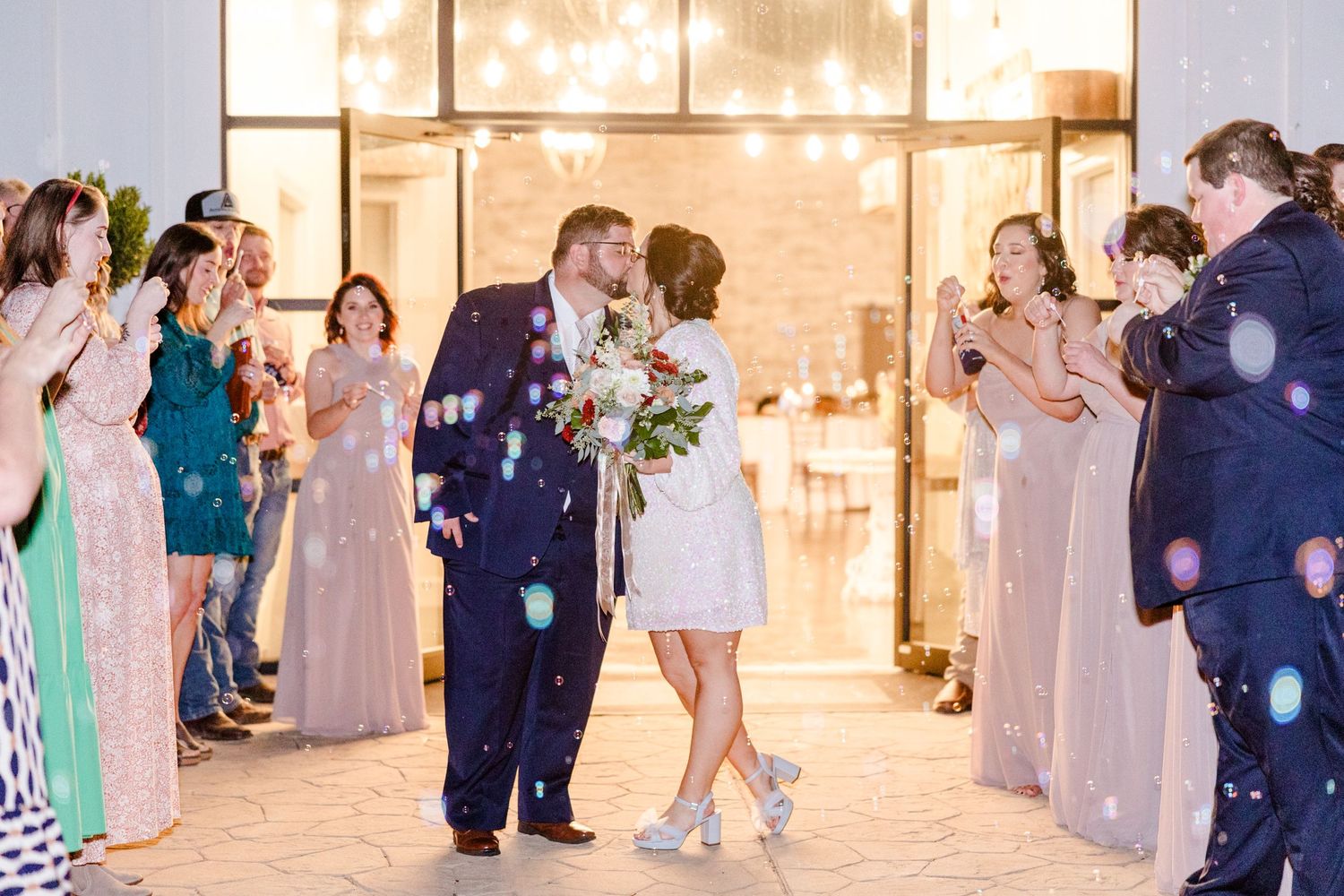 Joyful wedding exit with guests throwing confetti in an illuminated evening ceremony.
