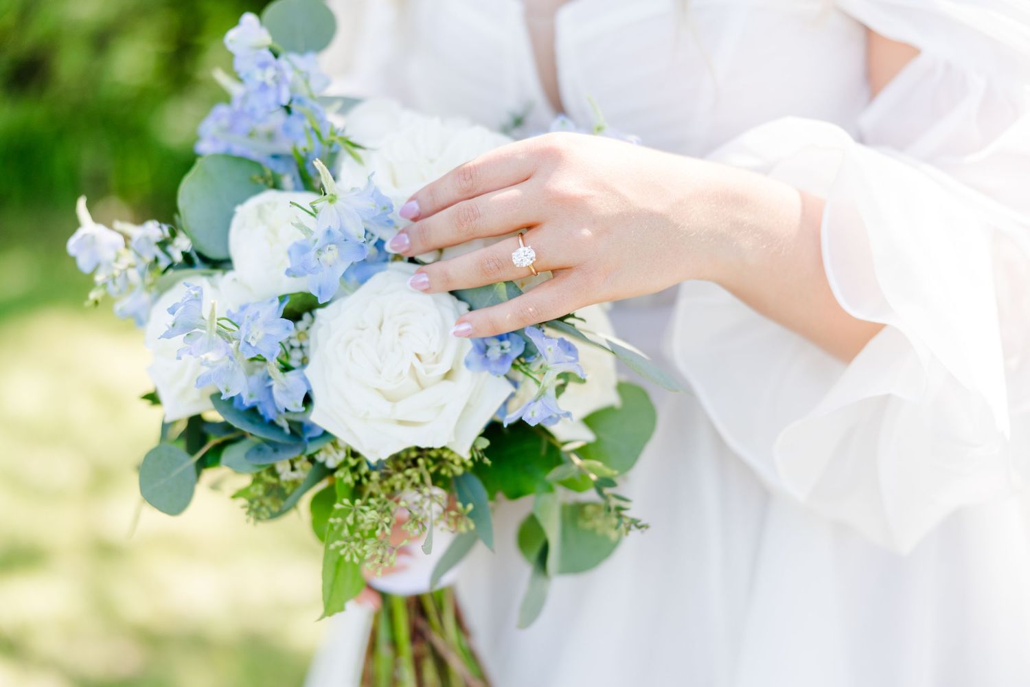 Elegant white and blue floral bouquet with delicate greenery held against a sunny outdoor backdrop.