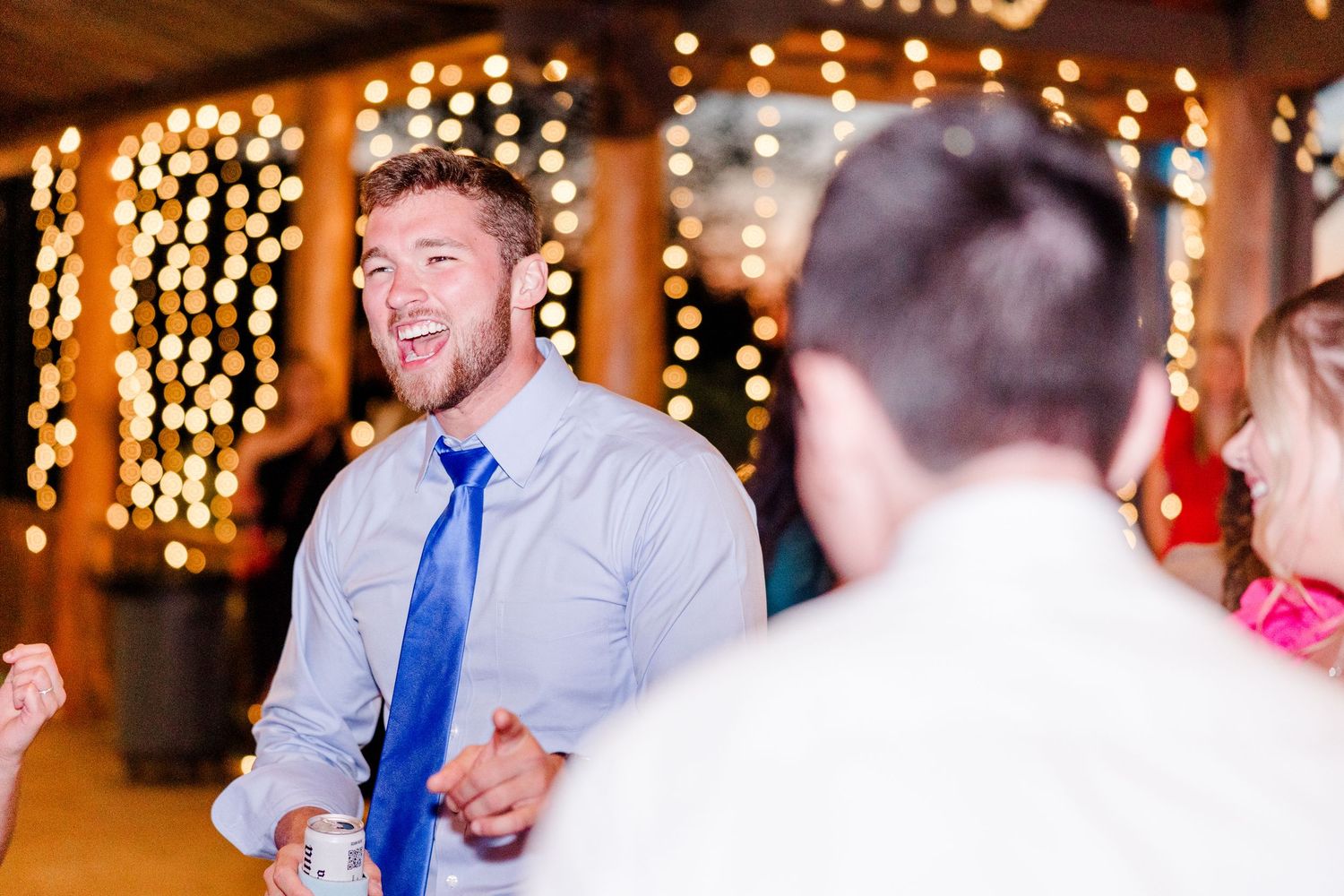 Wedding reception dance party with string lights creating warm ambient glow in rustic venue.