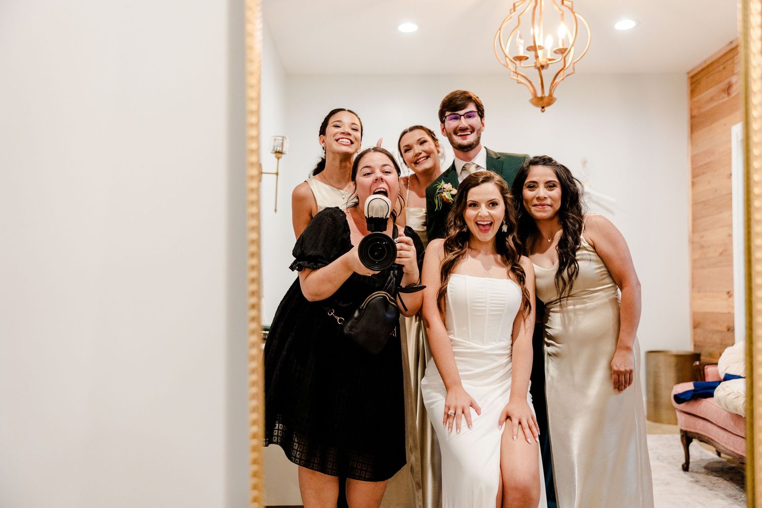 Group of friends posing for a mirror selfie at a wedding, bride in white gown with bridesmaids in formal attire.